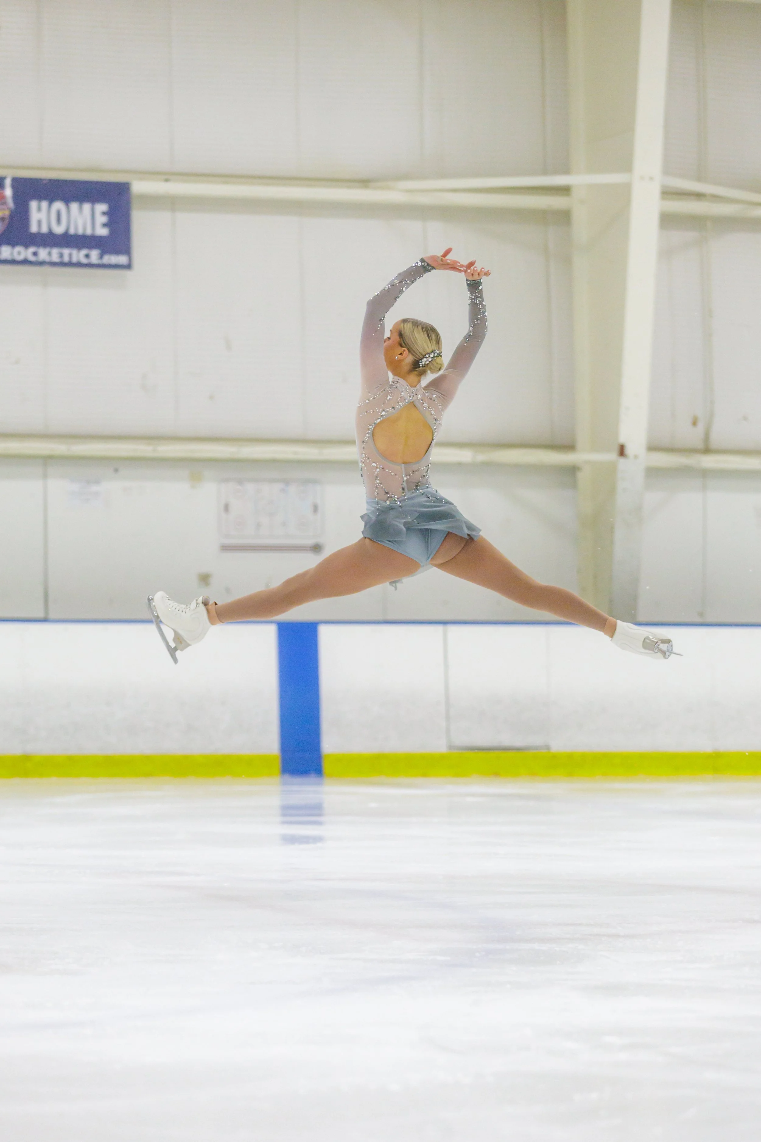 Figure skater in a sparkling costume performing a jump on an ice rink.