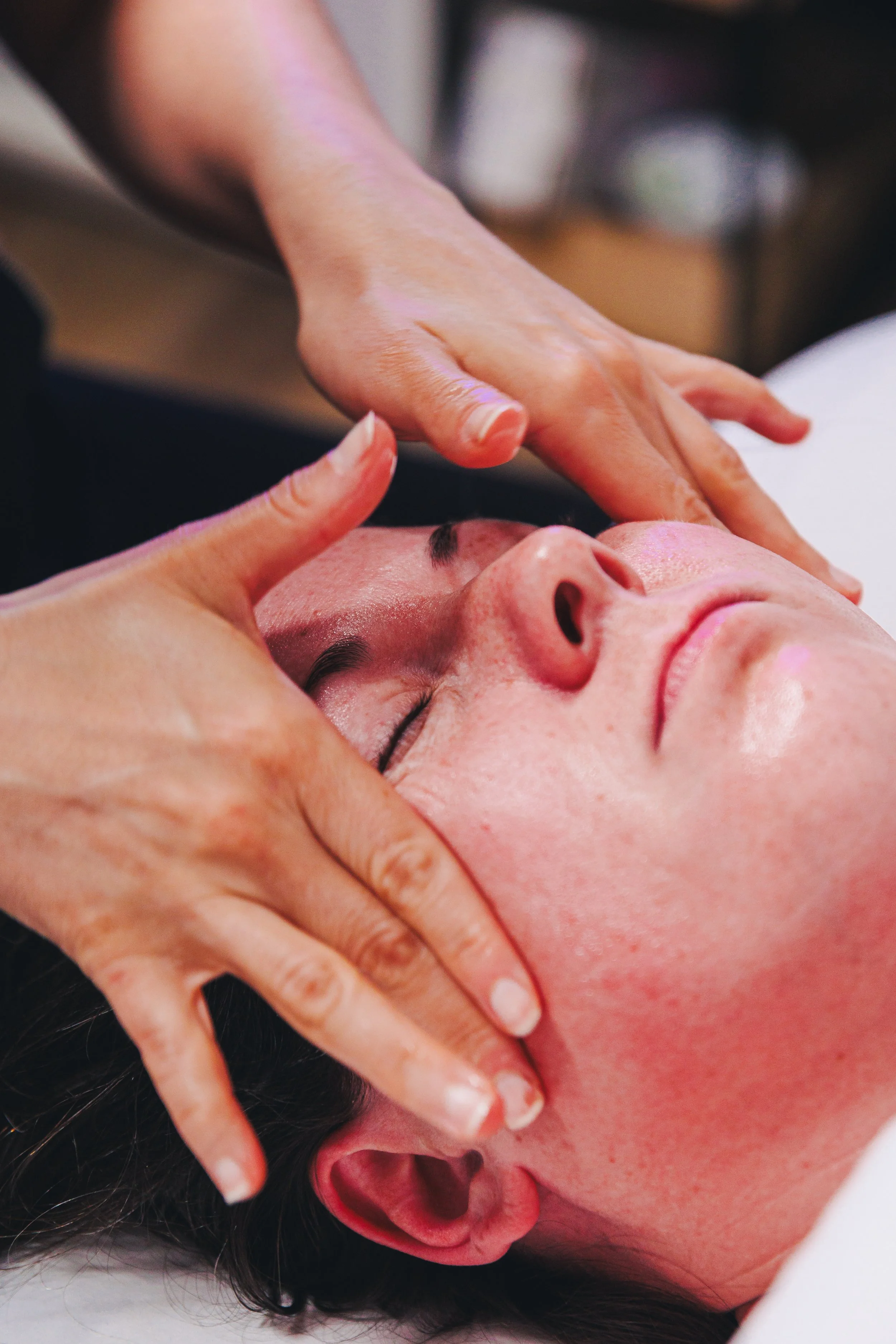 Person receiving a facial massage, lying down with eyes closed.