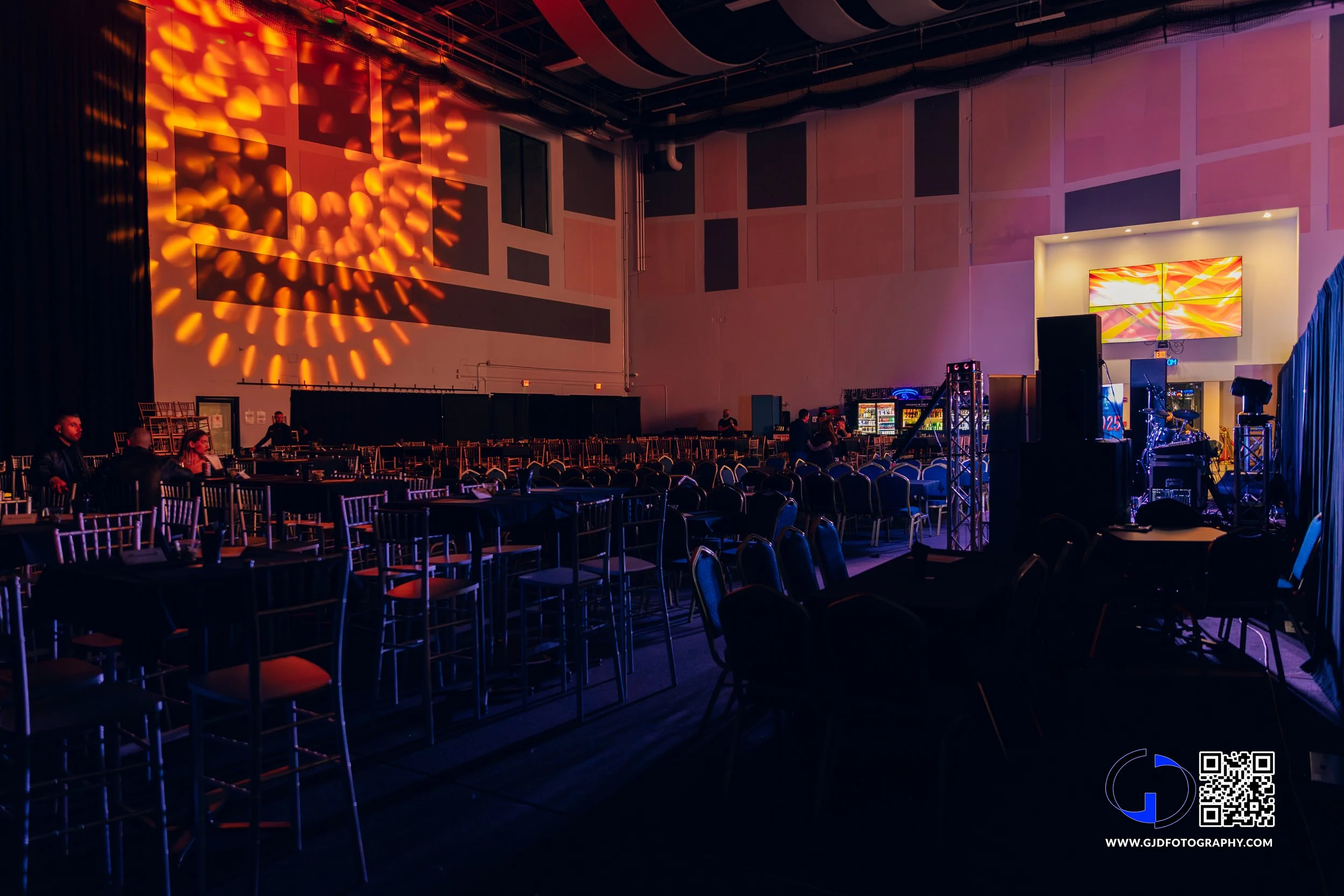 Empty event venue with a stage, lighting effects on the wall, and seating arrangements, ready for a performance or gathering.