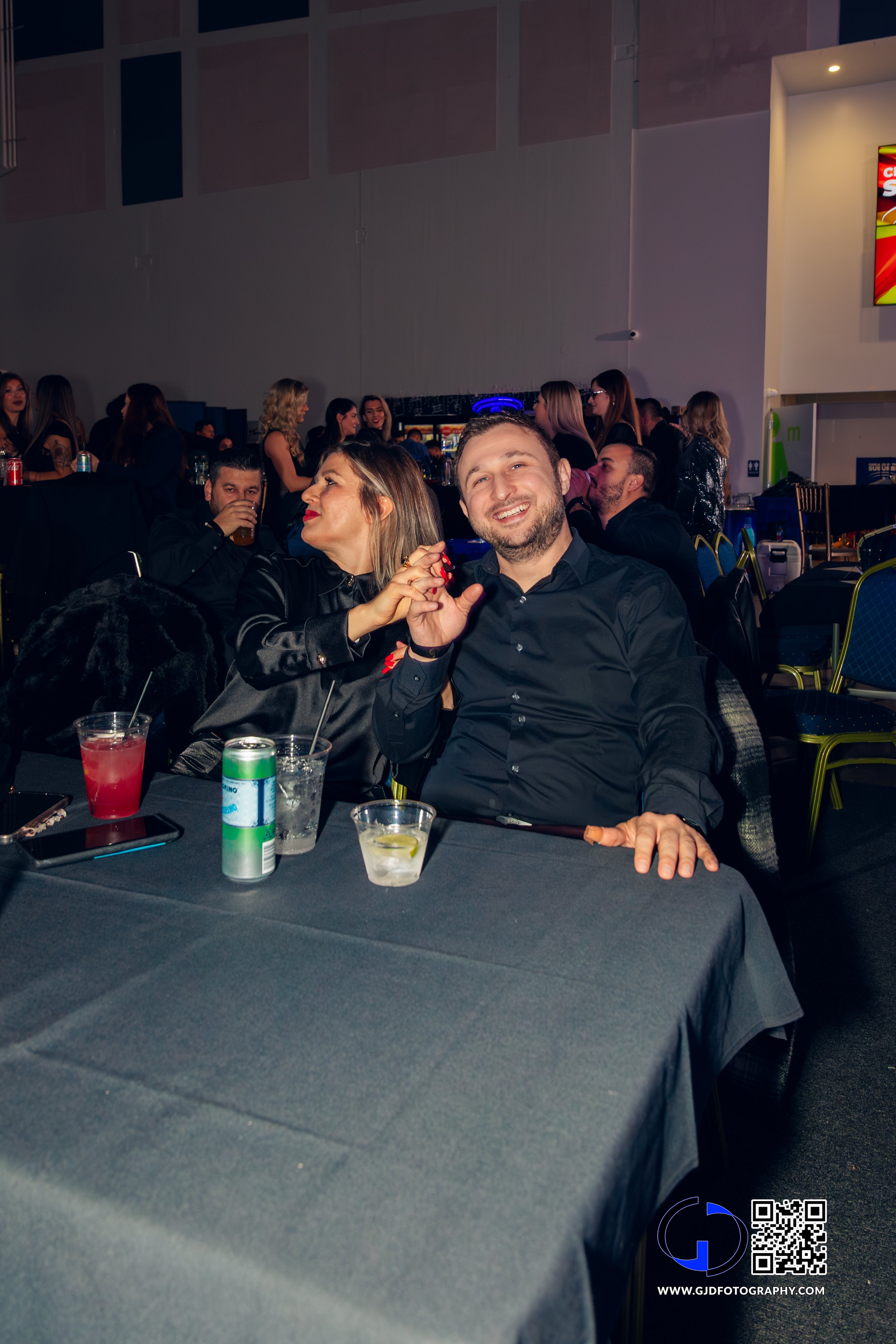 A group of people enjoying a night out at a party or social event, sitting around a table with drinks in a dimly lit indoor venue.