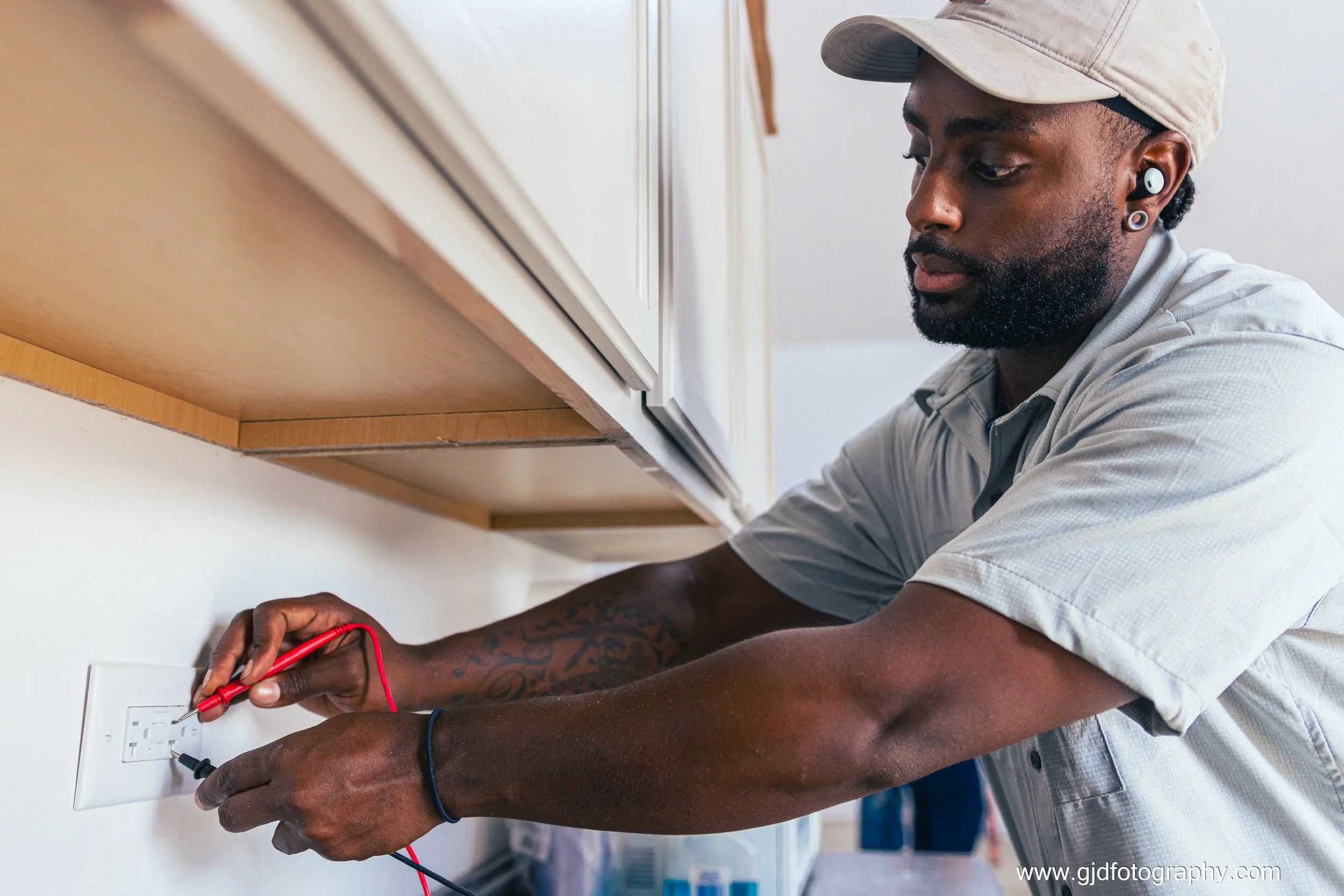 A man inspecting or repairing an electrical outlet using a multimeter and test probes.
