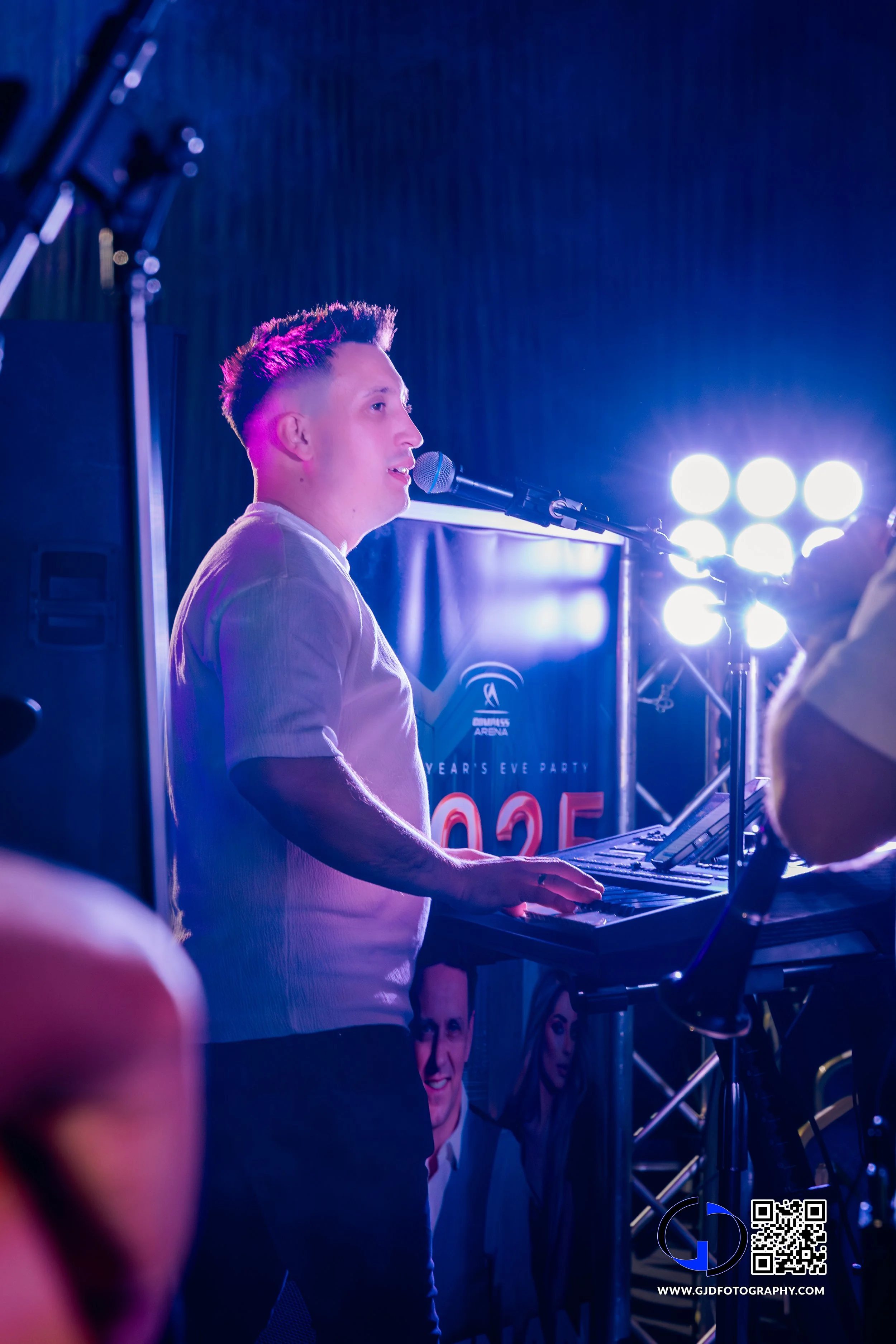 Young male pianist performing on stage at a New Year's Eve event, with bright stage lights behind him and a curtain in the background.