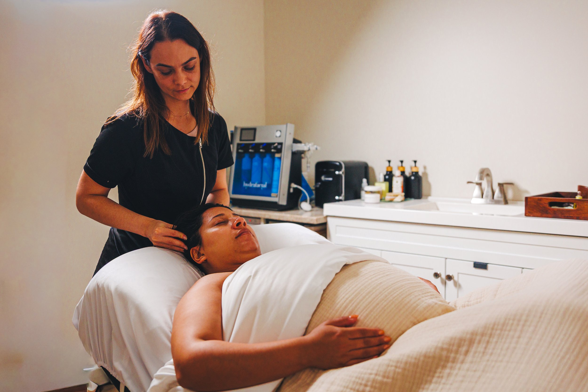 A woman receiving a head massage from a massage therapist in a spa or wellness room.