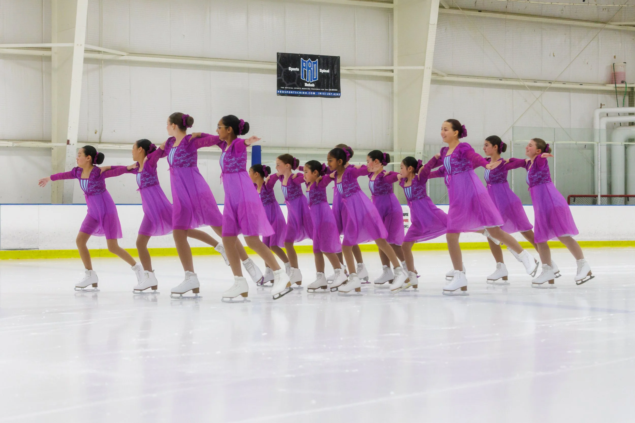 Group of young female figure skaters in purple costumes performing on indoor ice rink