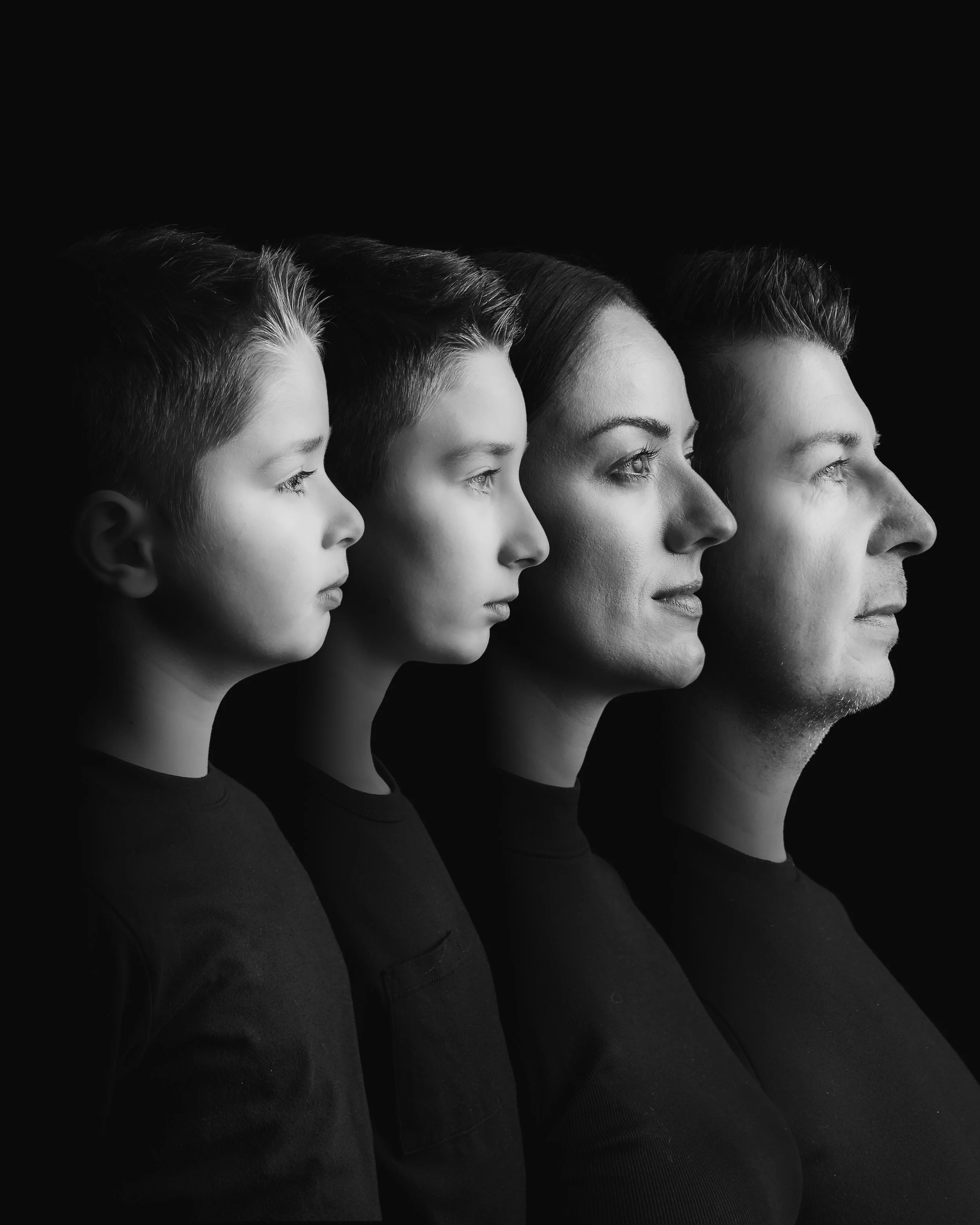 Black and white photo of four people, from a child to an adult, positioned in profile, with the faces aligned in a row against a dark background.