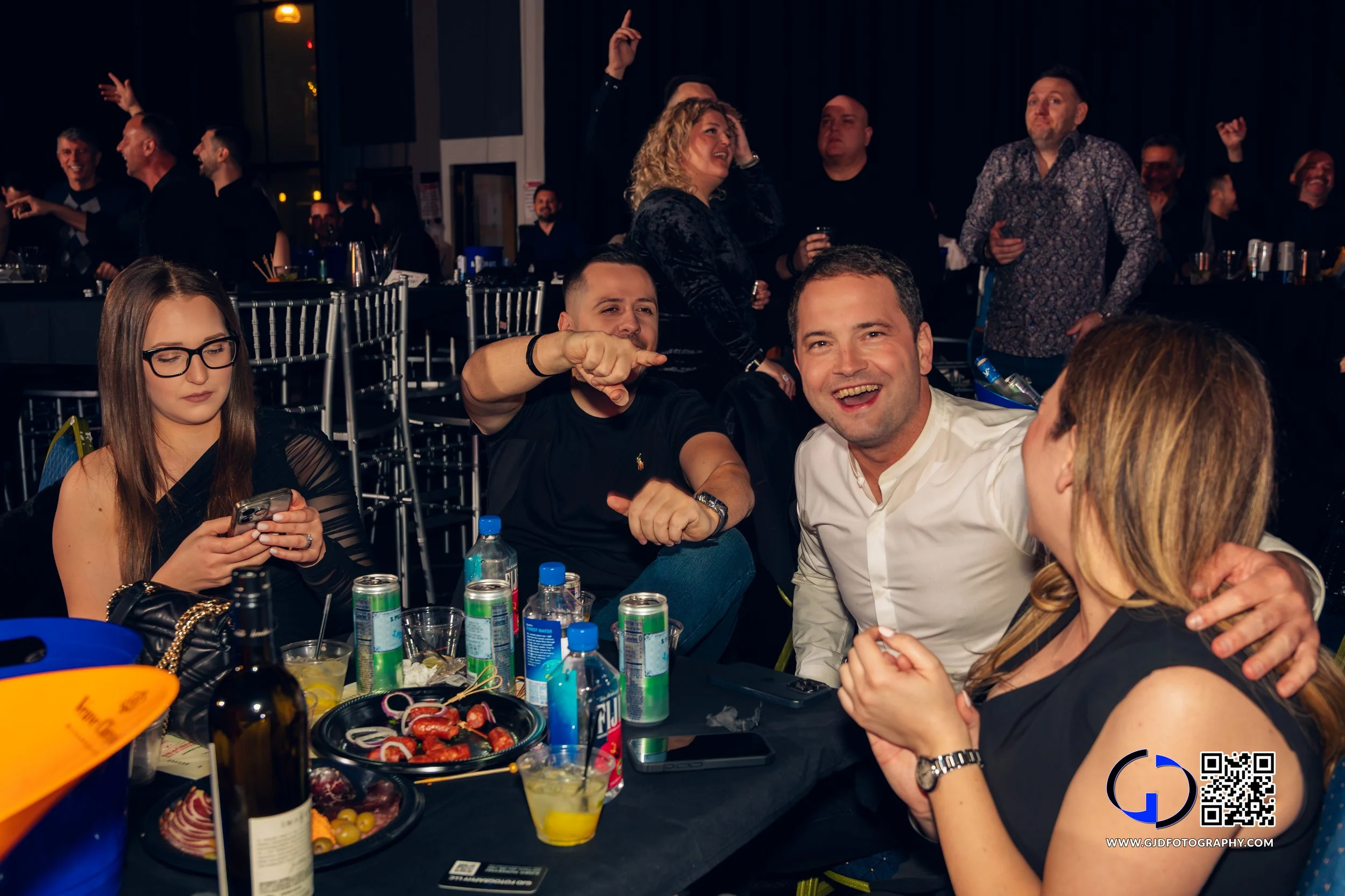 Group of people celebrating at a party, smiling and having fun, with snacks and drinks on the table.
