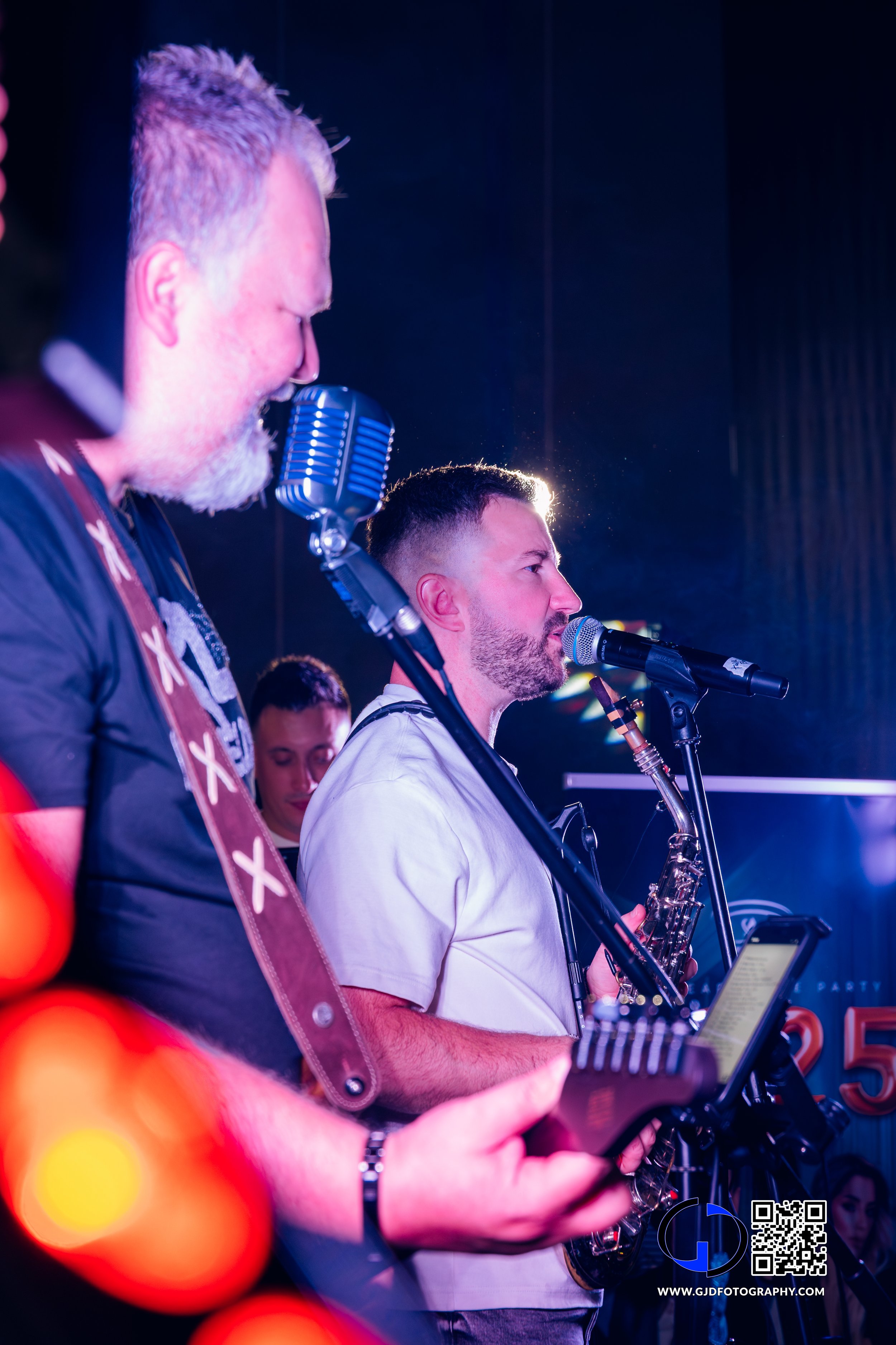 Two musicians performing on stage, one with a vintage microphone and the other with an electric guitar, during a live concert.