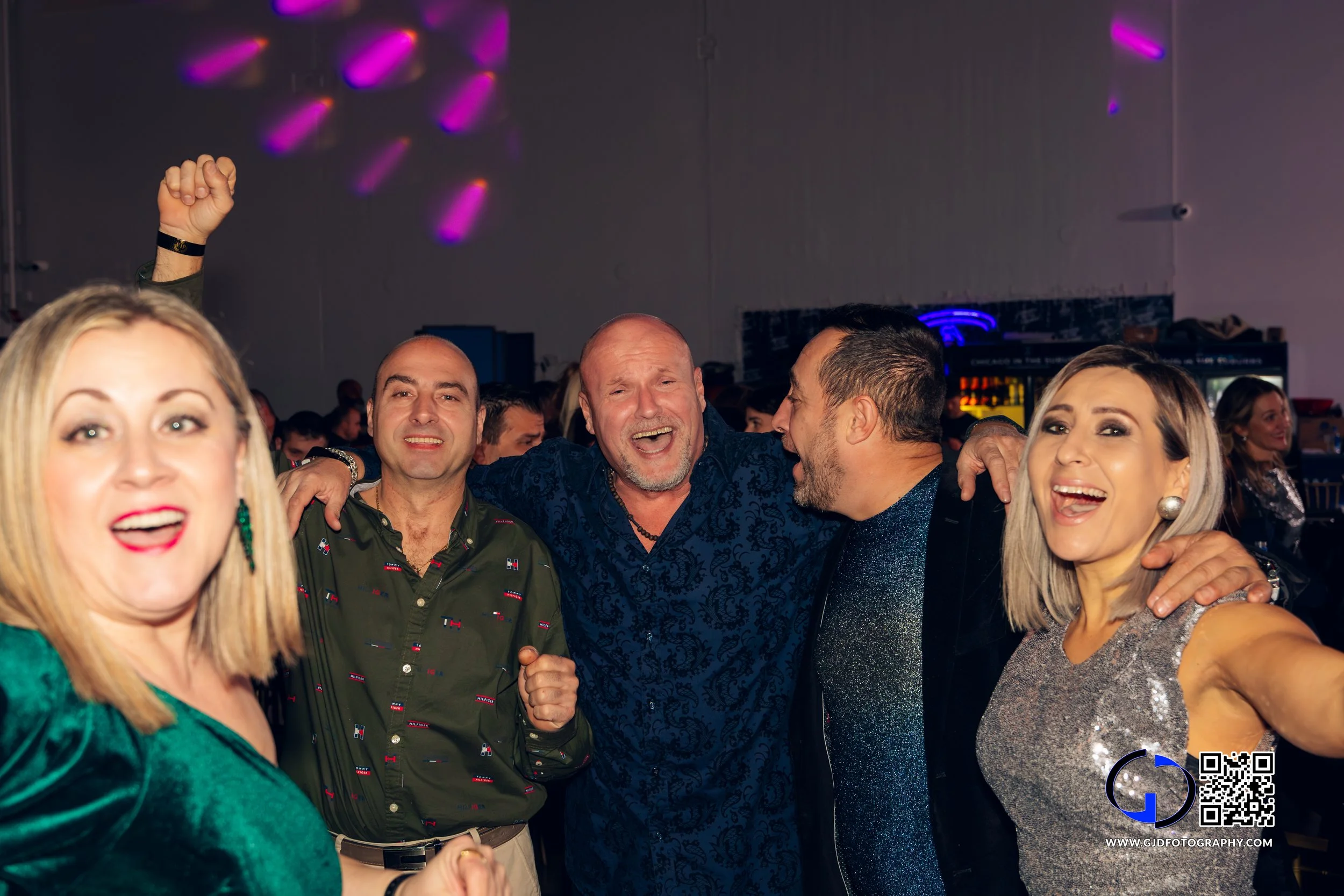 Group of five smiling adults celebrating and having fun at a party with colorful lights.