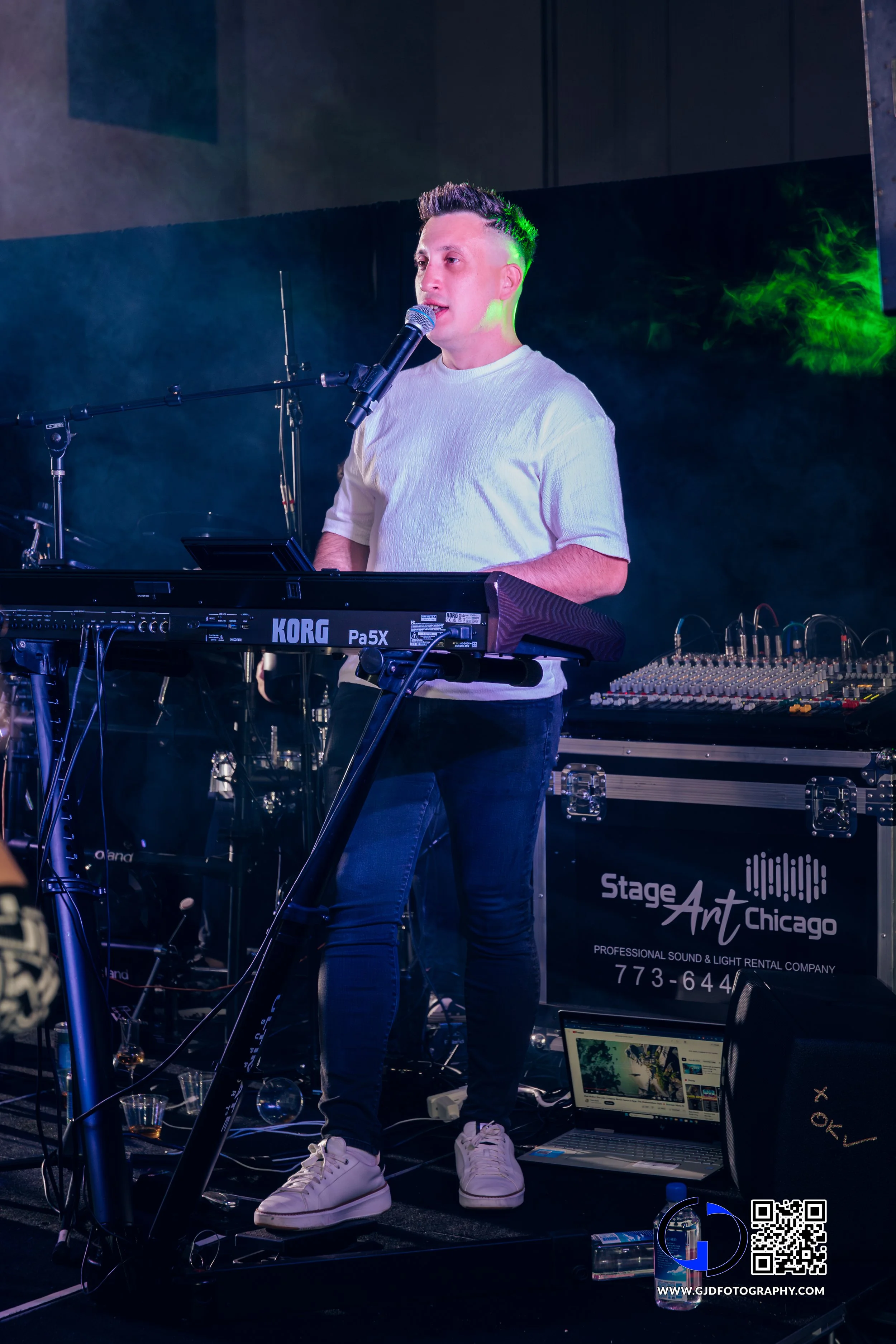 A male musician performing on stage with a keyboard and microphone