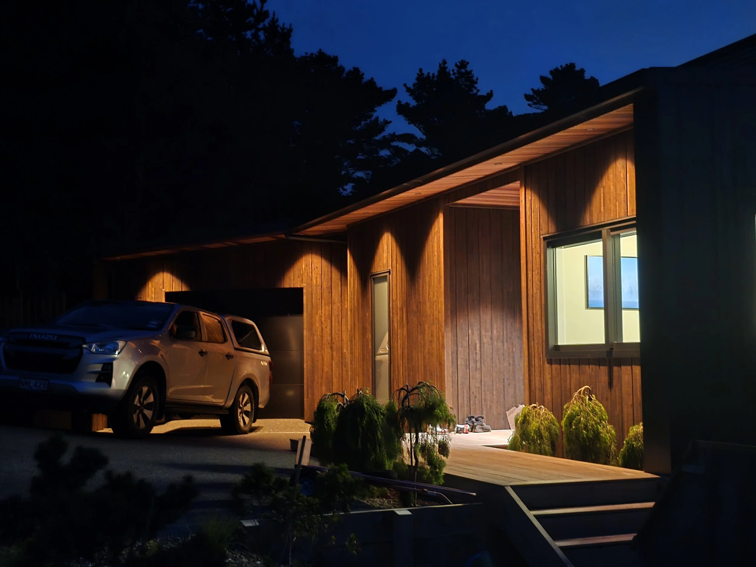 Modern house exterior at night with a parked SUV and illuminated porch.