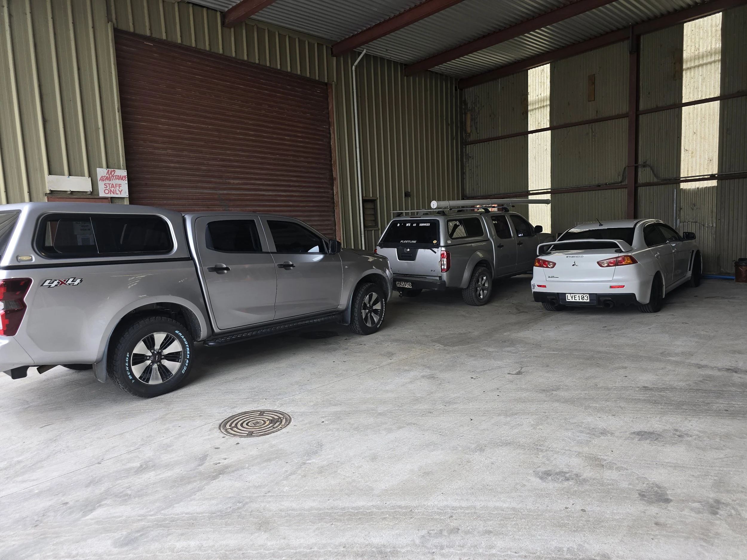 Indoor parking garage with three vehicles: two gray pickup trucks and one white car, parked near large metal doors.