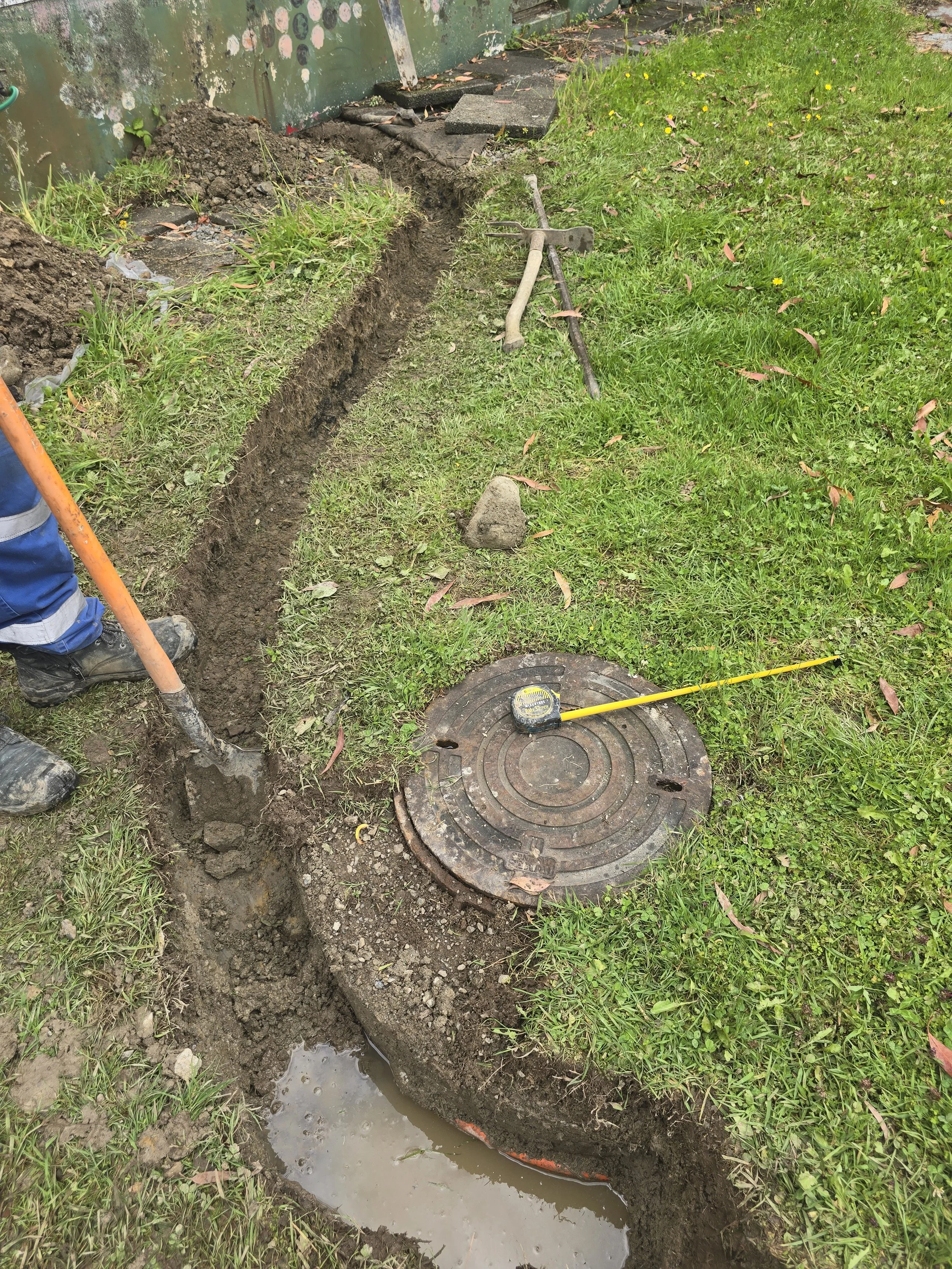 Trench with muddy water and worker near a manhole cover