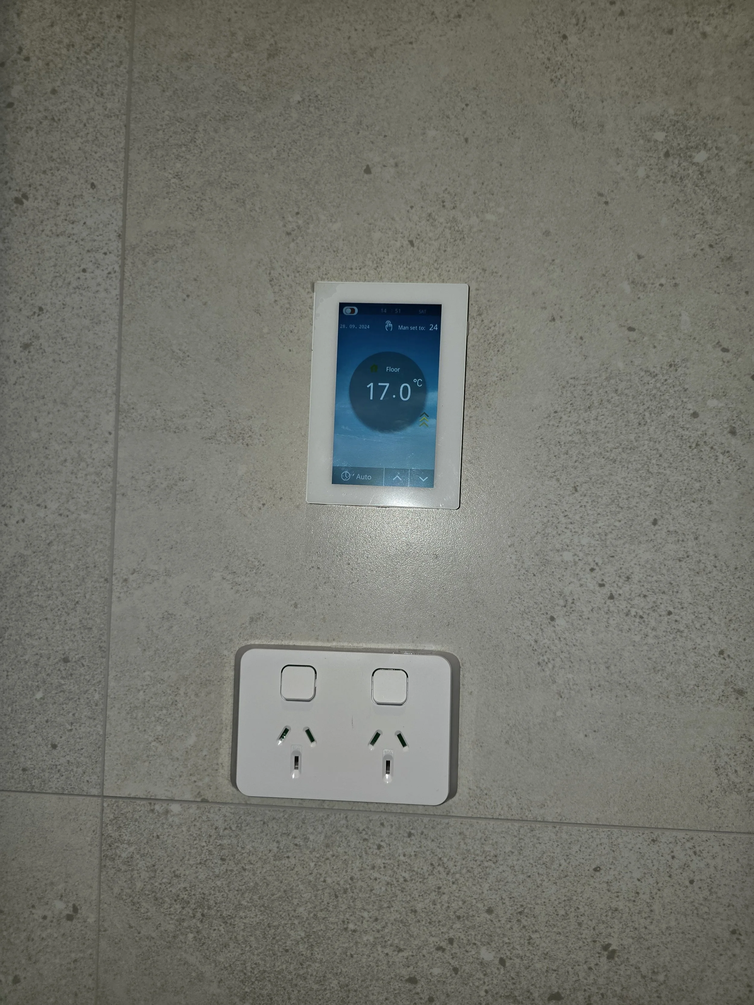 Wall-mounted thermostat displaying temperature and a double wall power outlet on a textured surface.
