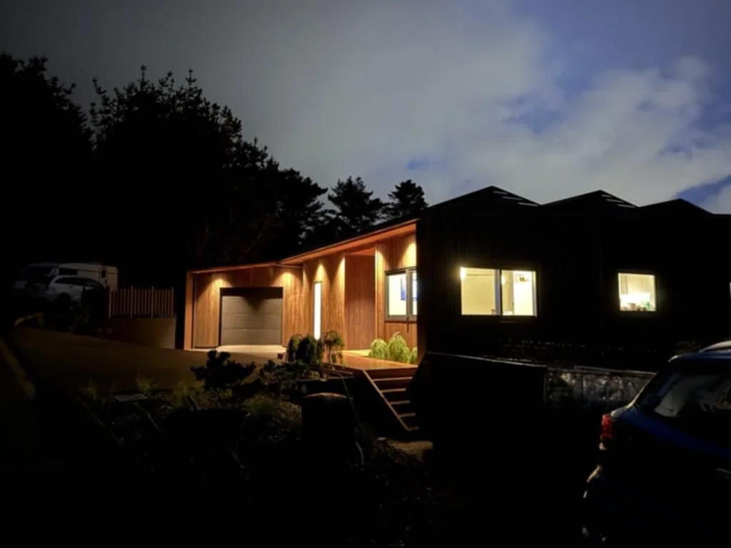 A modern house at night with lights illuminating the front entrance and windows.