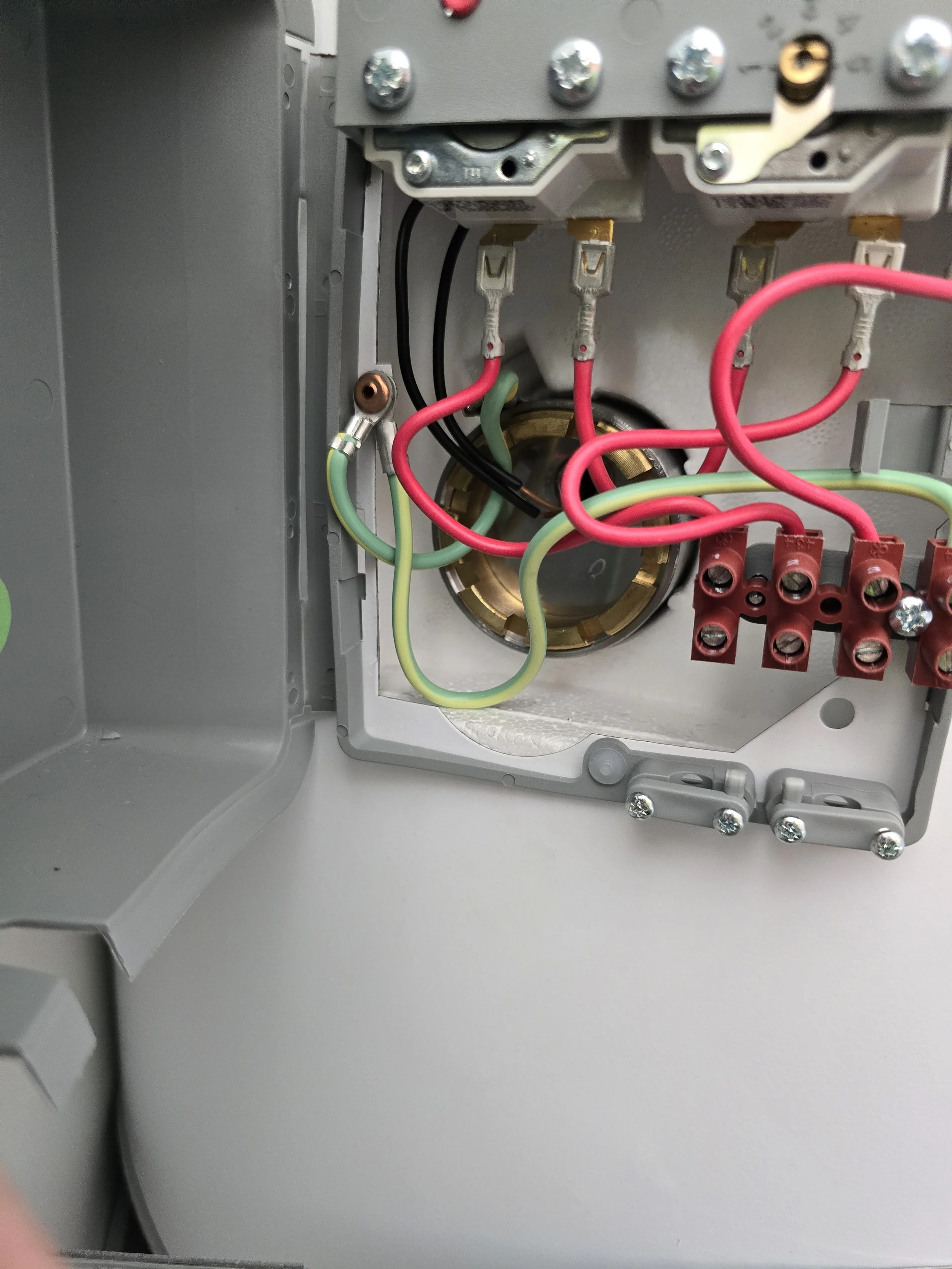Close-up of electrical box with wiring connections, featuring red, green, and black wires, secured by screws and connectors.