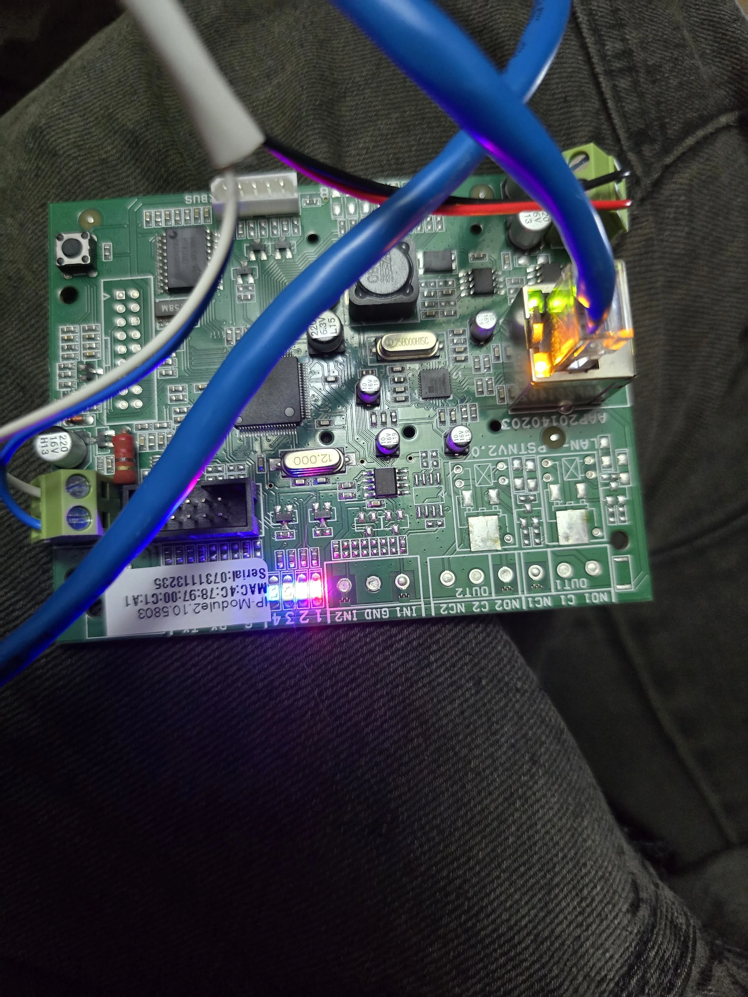 Close-up of a green circuit board with various electronic components, wires connected, and small illuminated LEDs, resting on a dark fabric surface.