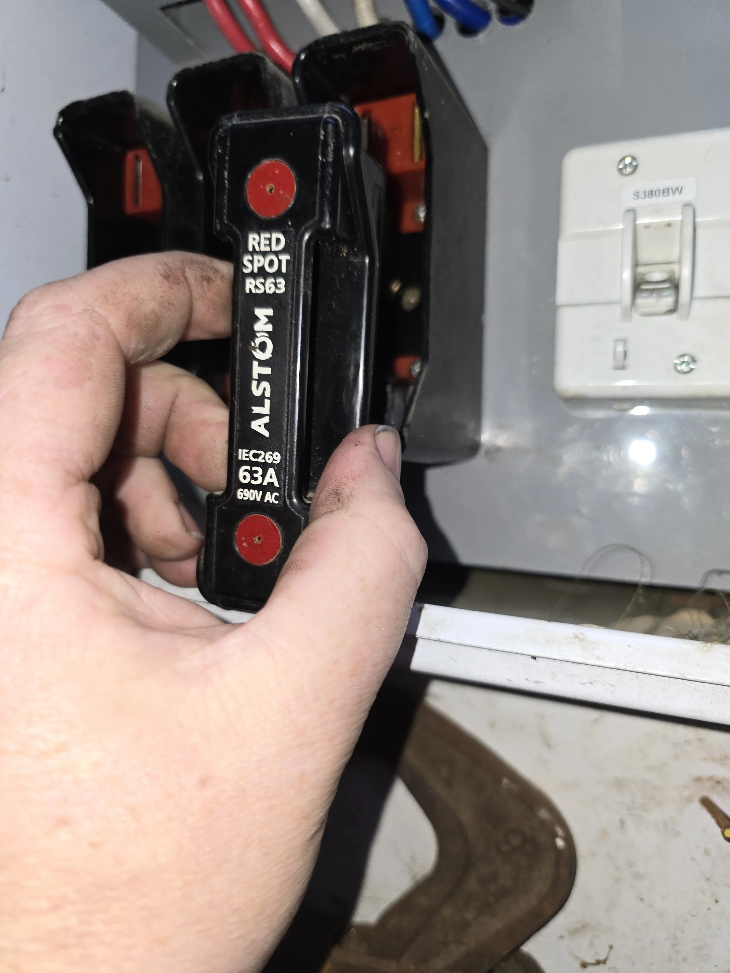 Person holding an Alstom Red Spot RS63 fuse, connected to an electrical unit.