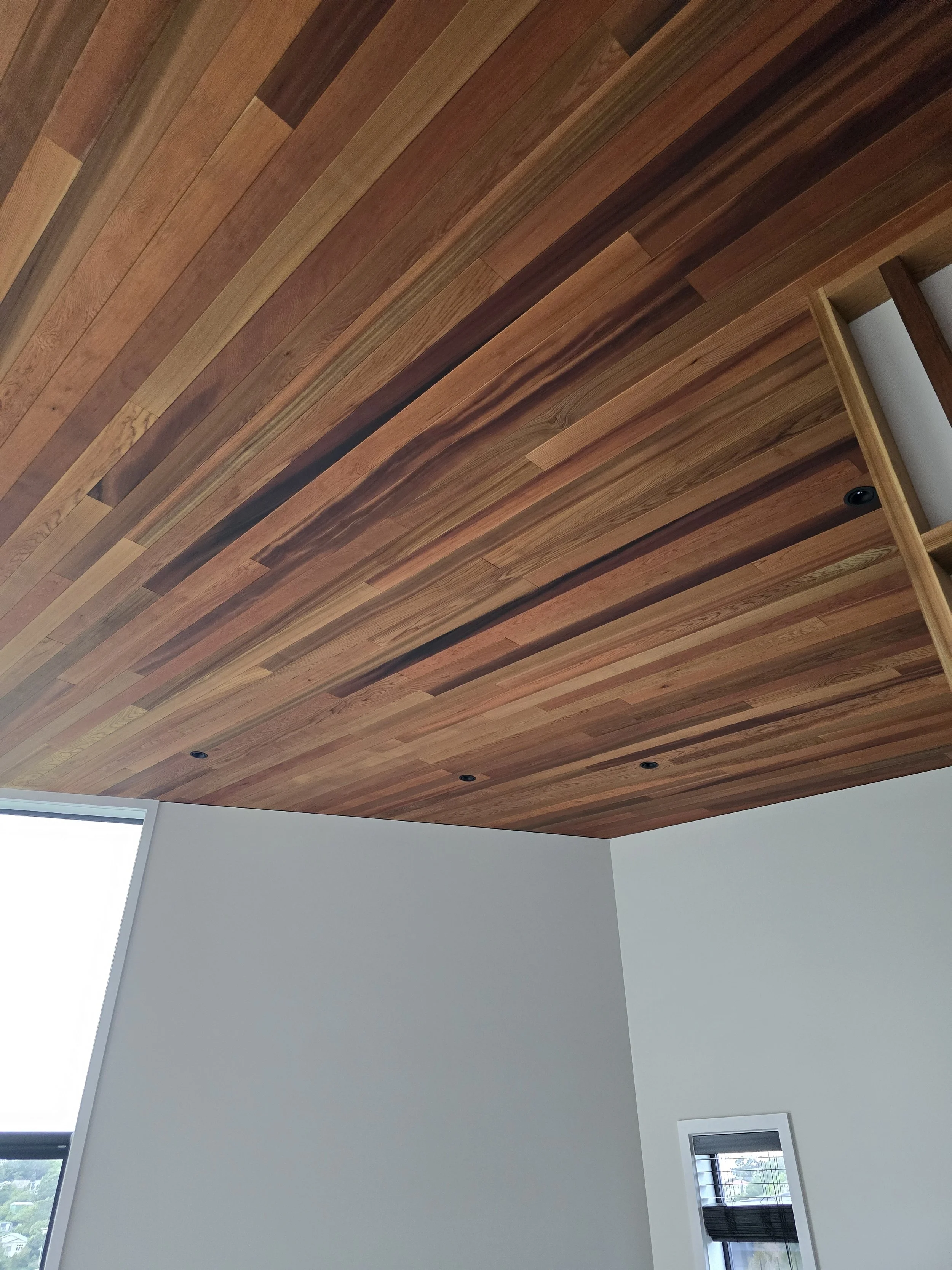 Wooden ceiling with recessed lights in a modern room with white walls.