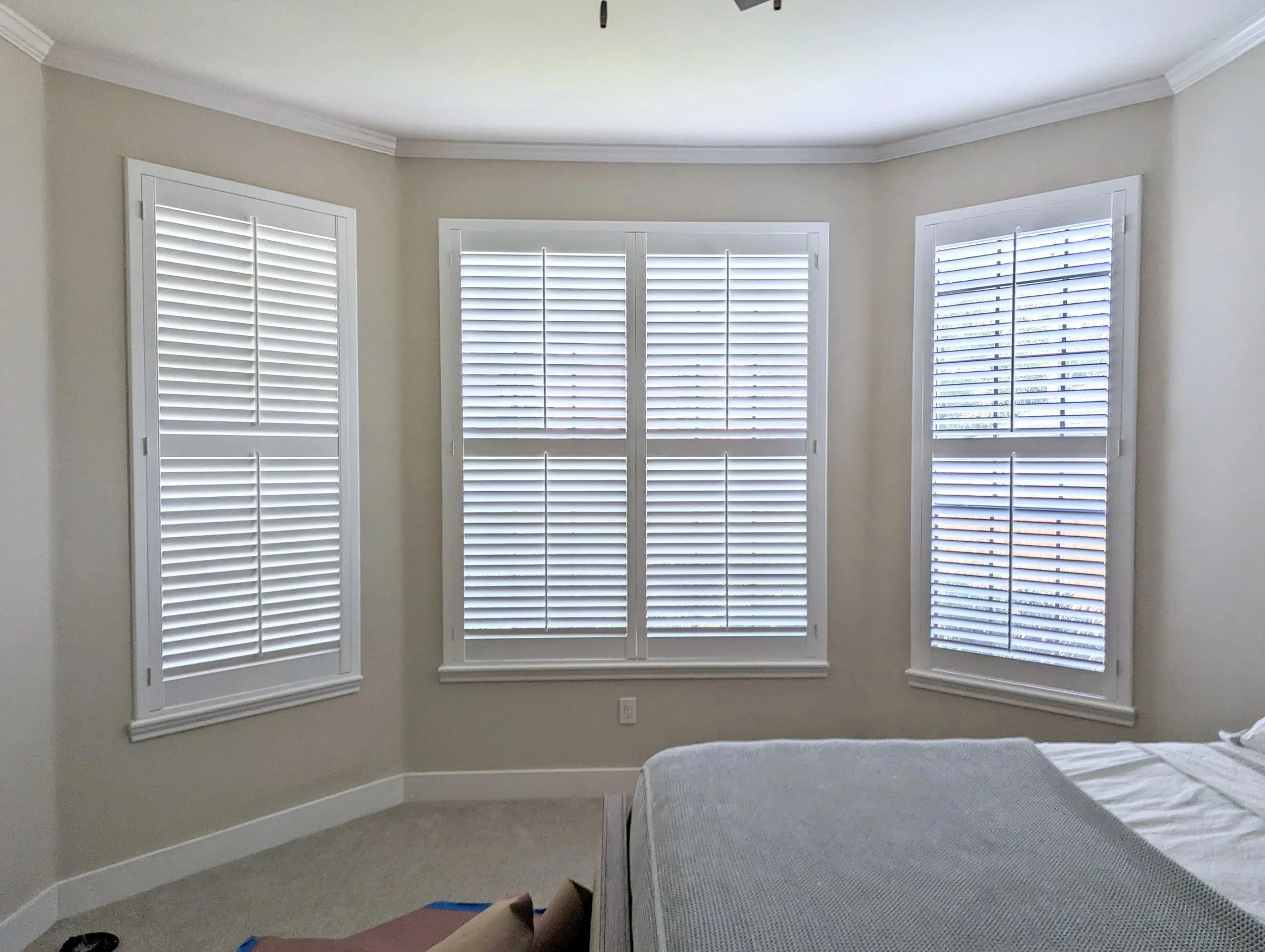 White plantation shutters across three windows with 2.5-inch louvers, a front tilt rod, 50/50 split tilt, and a Southwestern frame in a bedroom.