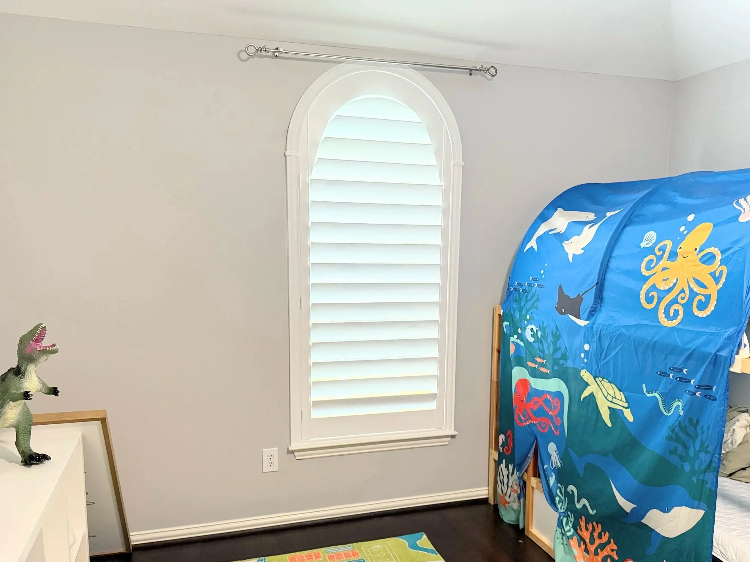 A full-arch plantation shutter with 4.5-inch louvers, hidden rear tilt, and a Traditional frame in a bedroom.