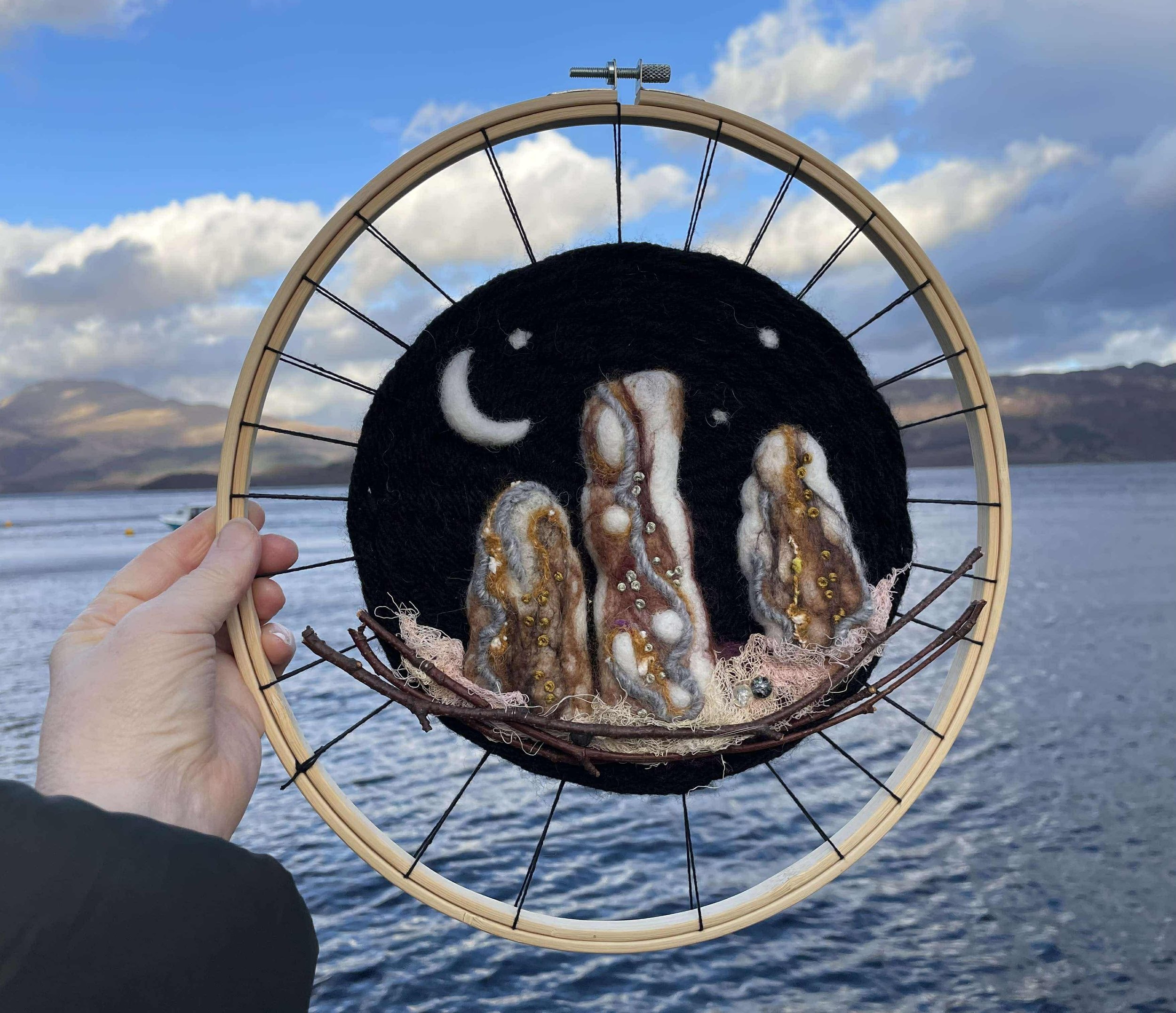 A circular woven artwork inspired by Loch Lomond, featuring a needle-felted standing stone made with natural and recycled materials. Handmade, and uniquely Scottish sustainable, and uniquely Scottish