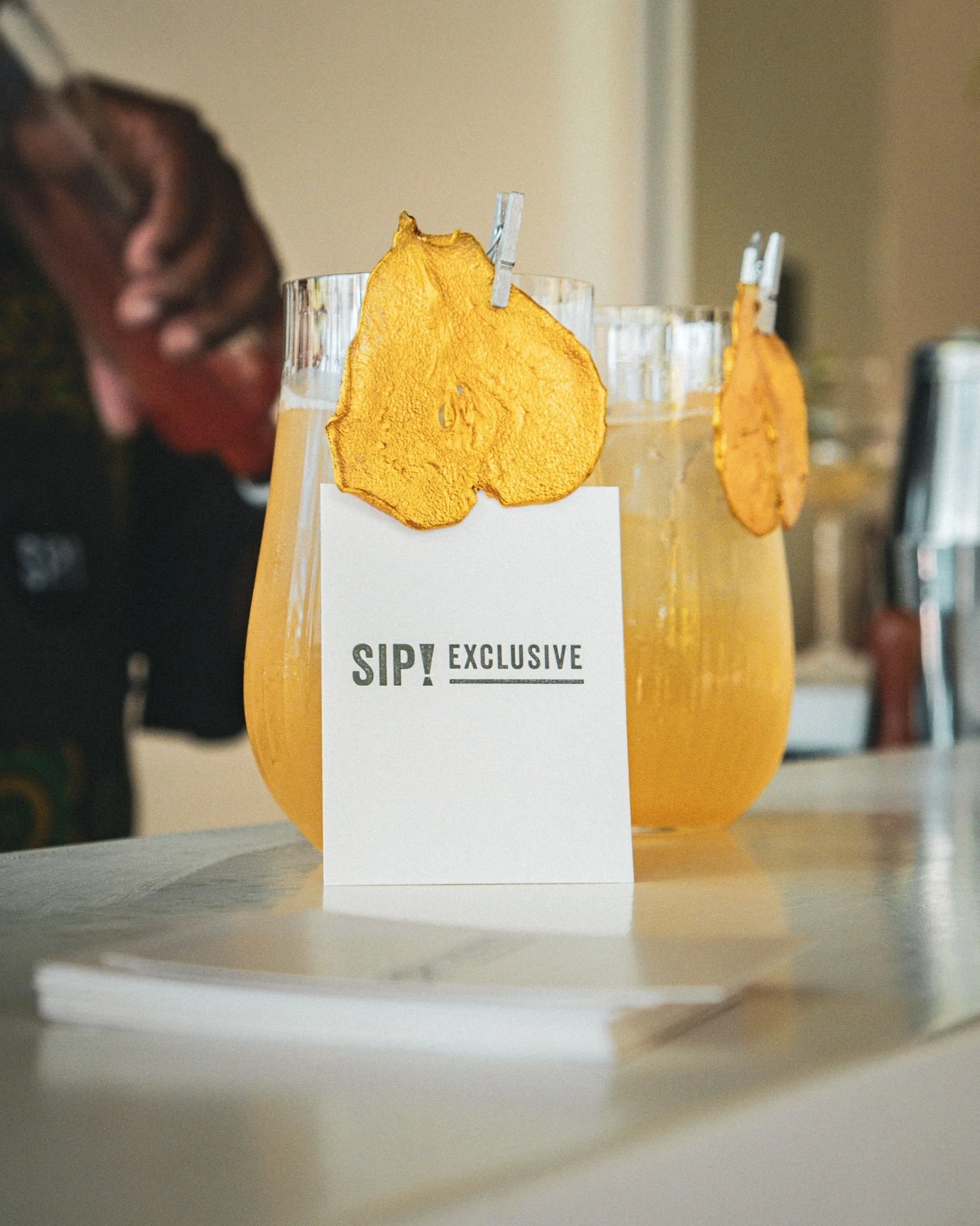 Beautiful cocktail in a glass with bains and pear juice plus a ginger syrup with a golden pear garnish and a SIP Card.