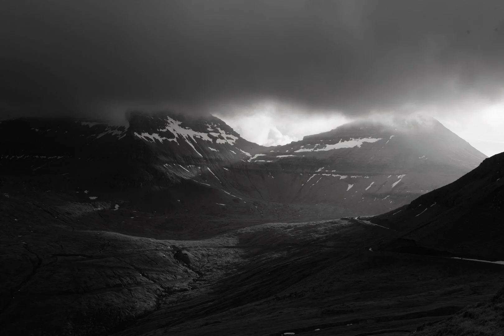A black and white photo of a mountain landscape with dark clouds overhead.