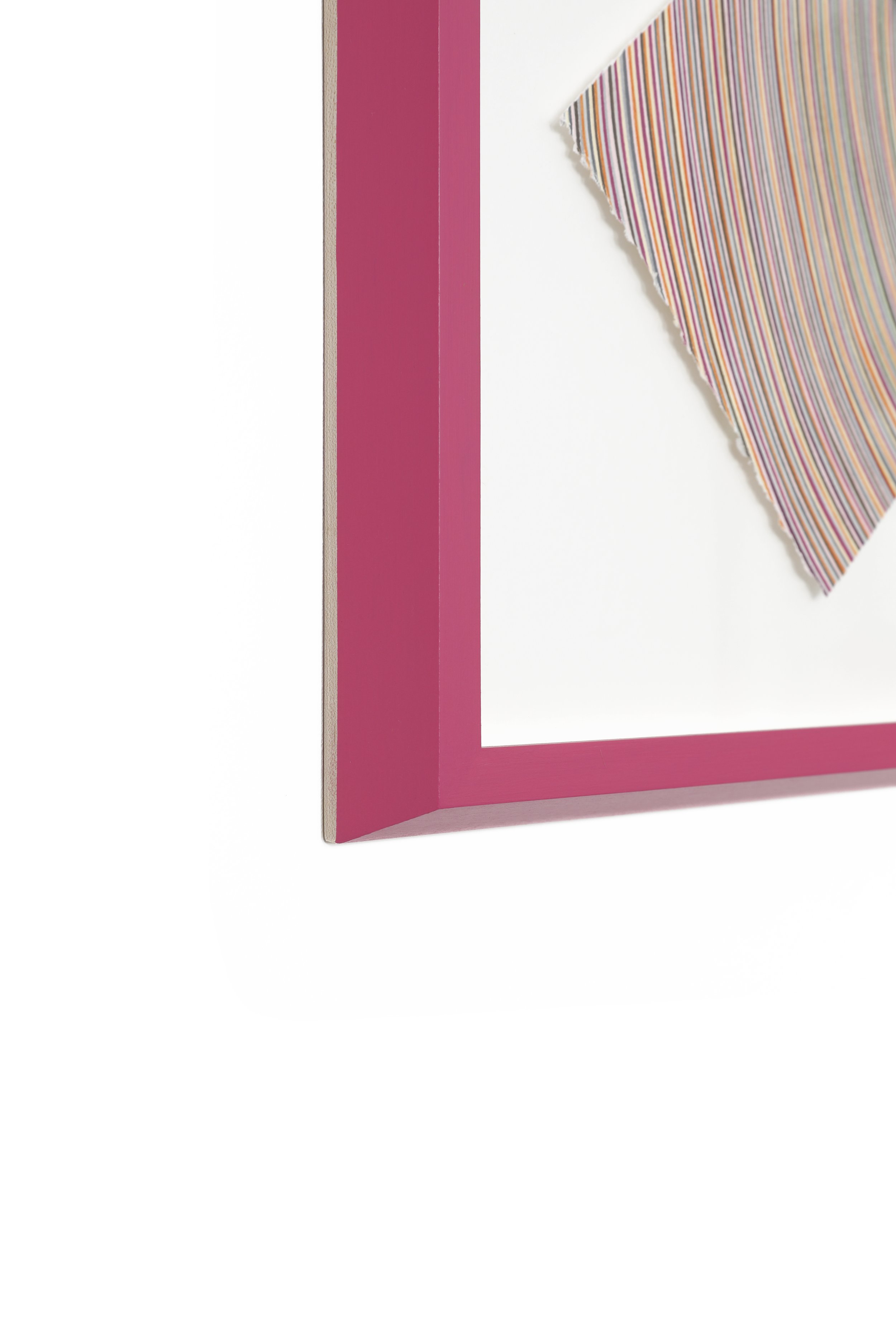 Close-up of a corner of a pink picture frame with a colorful striped fabric inside.