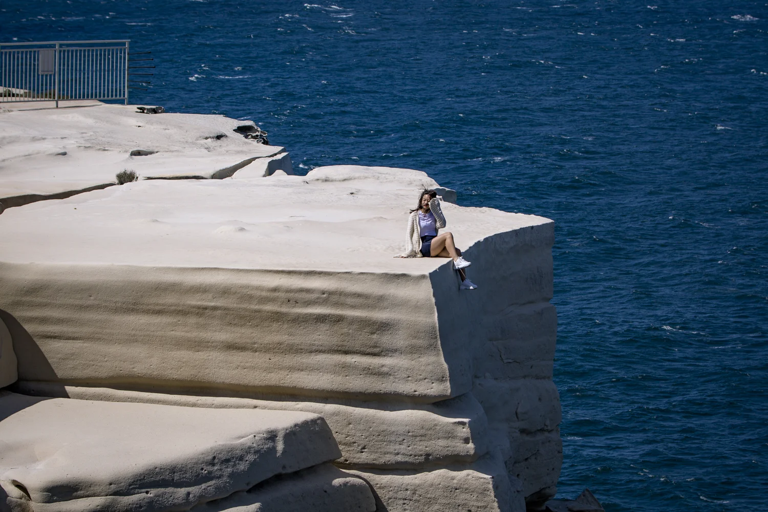 Just sit over there! She sits on the edge of the rock even taking a moment to take a photo looking down some 30 metres to a the rocky ocean ledge below.