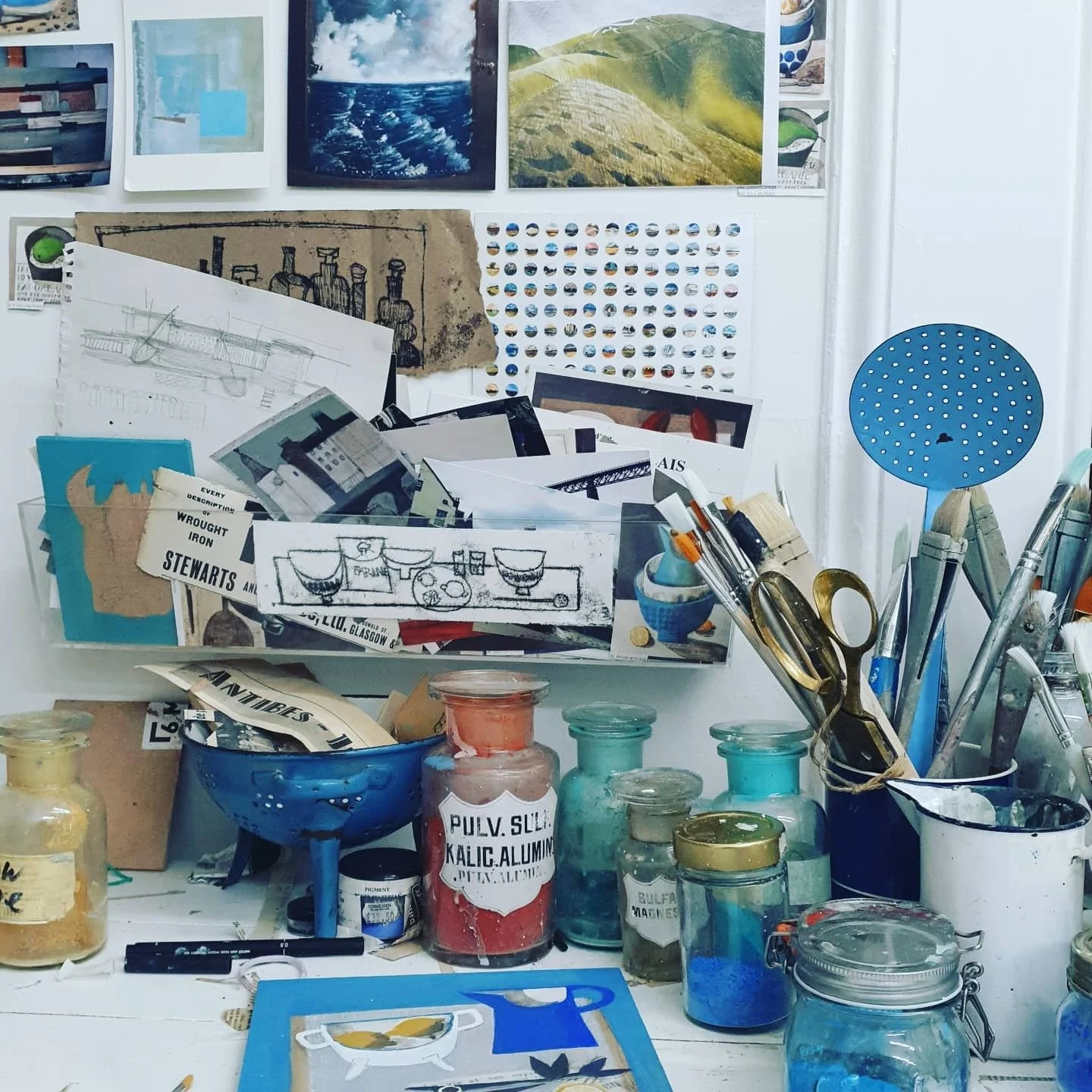 Astrid Trügg artist studio materials with pigment jars, brushes, sketches and collected painting references.