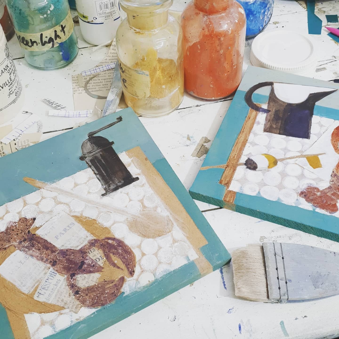 Mixed media painting panels in progress with gesso, pigment jars, collage and studio brushes.