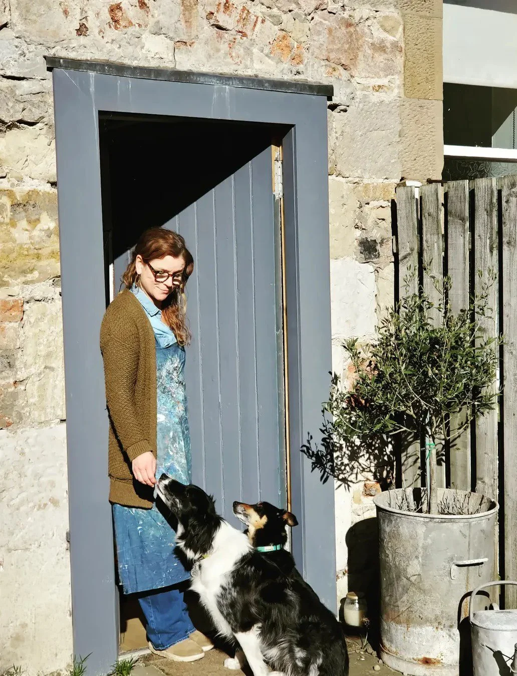 Scottish artist outside a stone studio doorway with two dogs, introducing Astrid Trügg’s studio process.