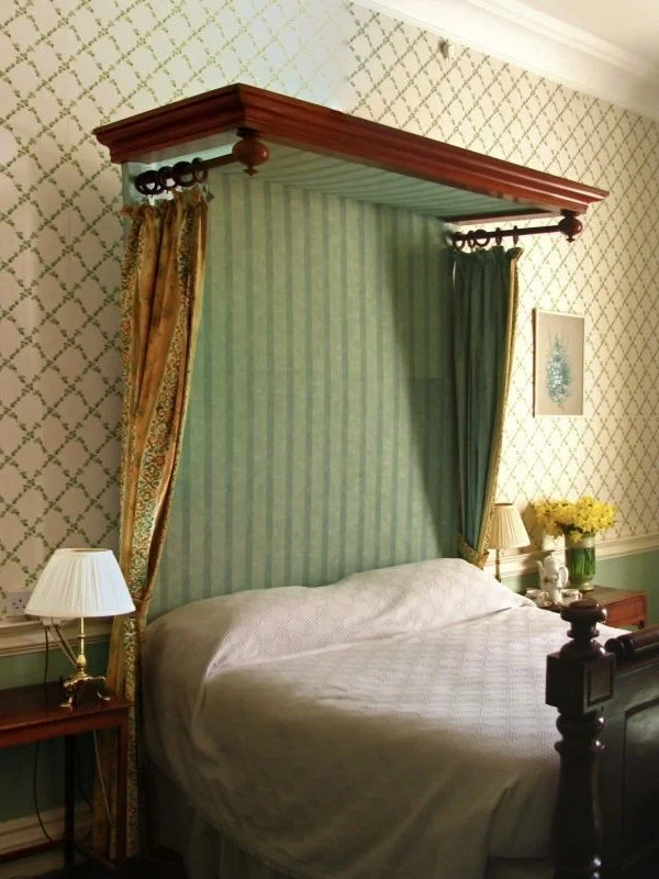 an ornate four poster bed, with a pale green curtained backdrop, lighting and flowers in bedroom accomodation at Coopershill House, Sligo, west of Ireland
