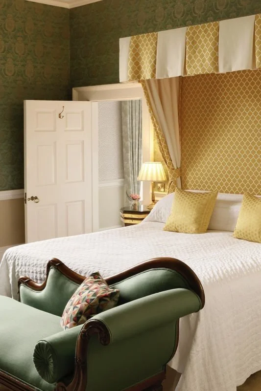 An ornate bed, with yellow patterned canopy and green walls, with green chaise longue at Coopershill House, Sligo.
