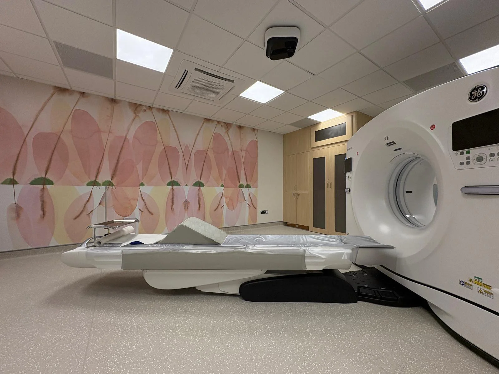 An MRI scan machine in a Limerick hospital, with subtle warm pink artwork on the background wall. The hospital architect chose Irish artist Tracy Sweeney to create artworks that supported the function of the clinical space.