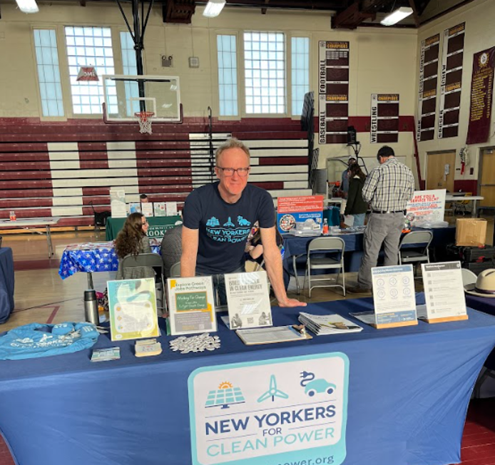 Man tabling with "NY for Clean Power" in school gym. papers and information on the table.