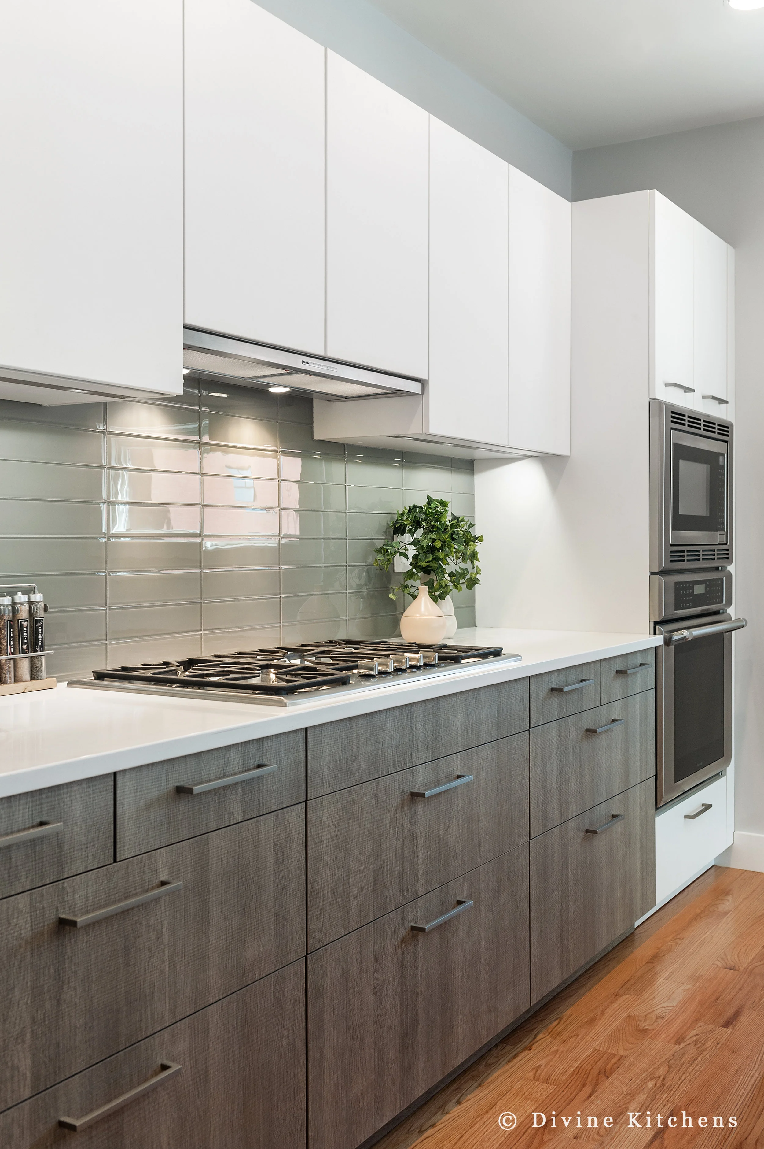 Modern kitchen with matt white, flat-panel cabinets and cambria countertops with a waterfall edge on island, green subway tile backsplash, wall oven.