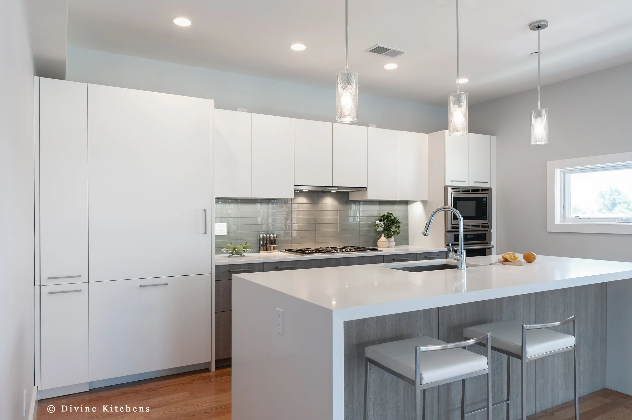 Modern kitchen with matt white, flat-panel cabinets and cambria countertops with a waterfall edge on island, green subway tile backsplash, wall oven.