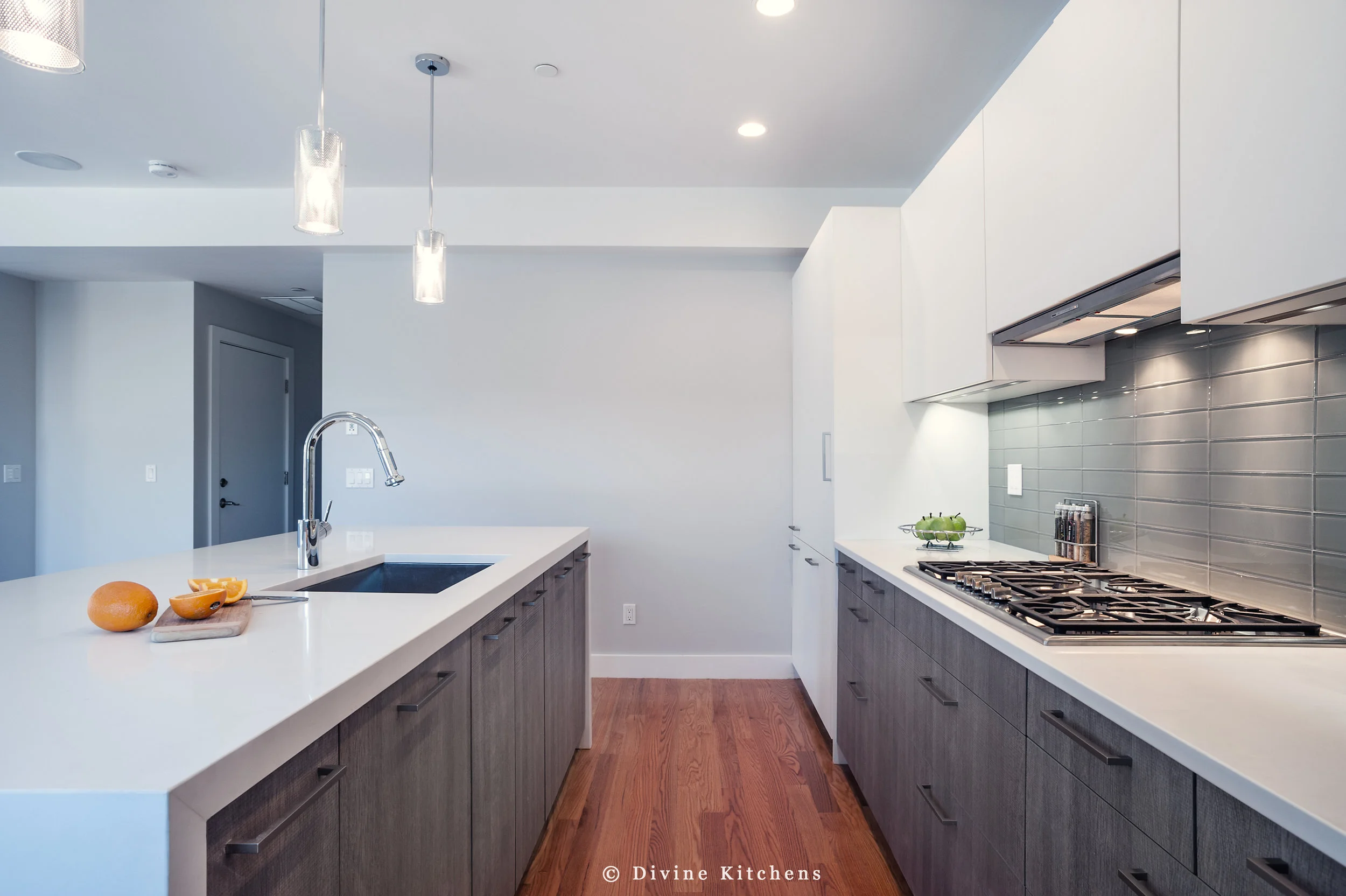 Modern kitchen with matt white, flat-panel cabinets and cambria countertops with a waterfall edge on island, green subway tile backsplash, wall oven.