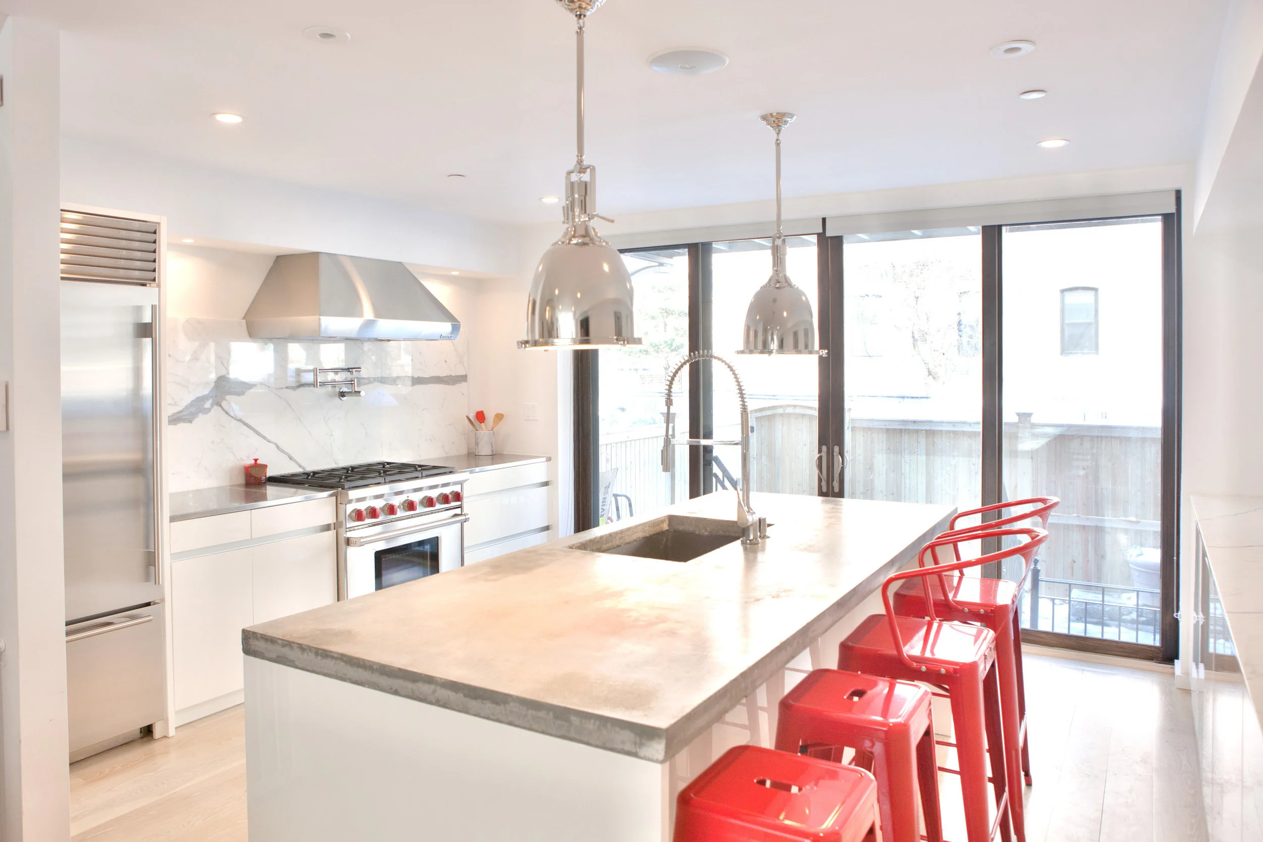 white modern kitchen with concrete island countertop. Red, modern barstools and matt white, Leicht kitchen cabinets with a griprail opening system. Wolf oven and range.