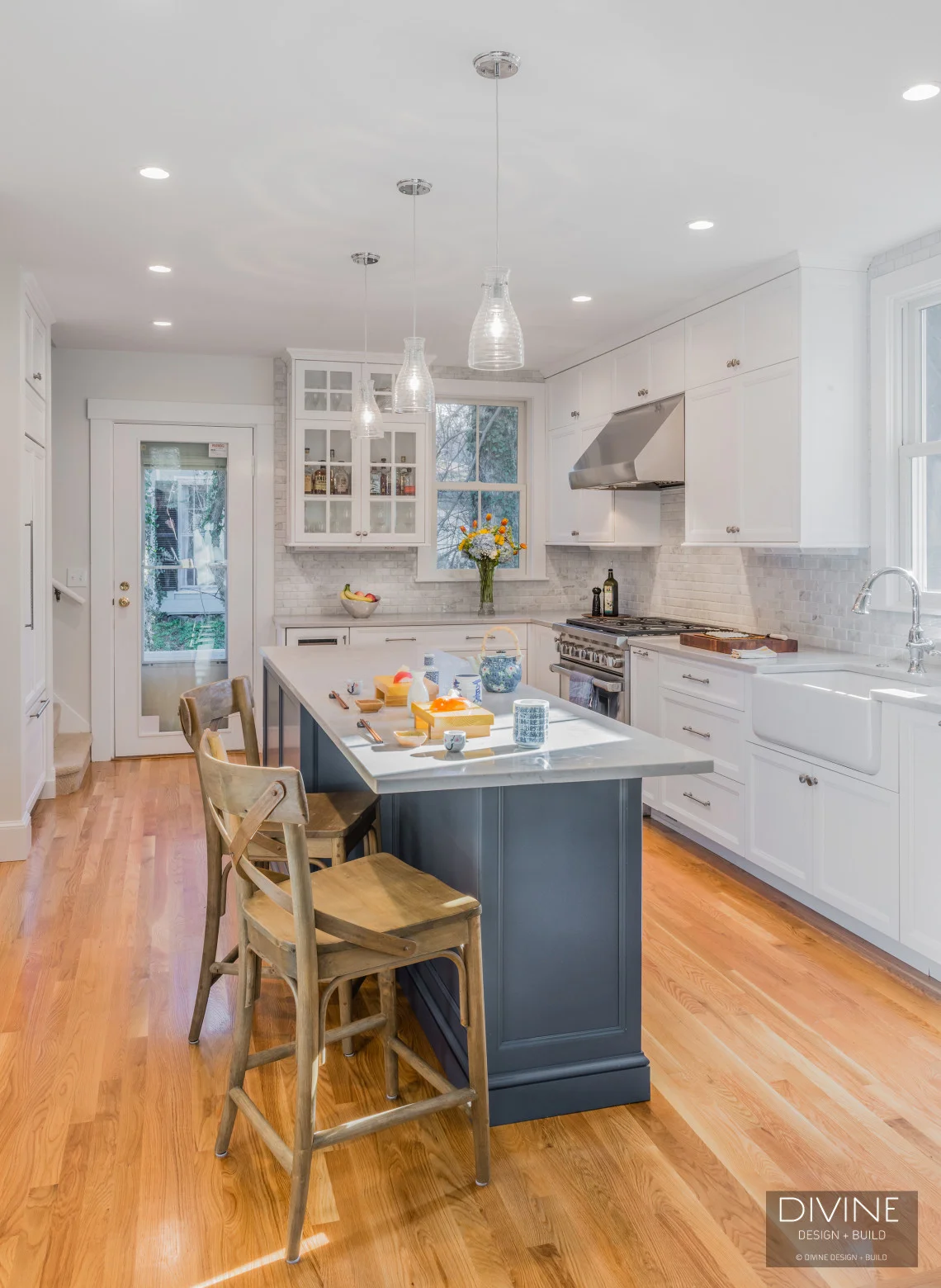 white transitional kitchen with white shaker cabinets and brushed nickel accessories. cambria calacatta island countertop with blue cabinetry. Wolf appliances. mosaic subway tile backsplash