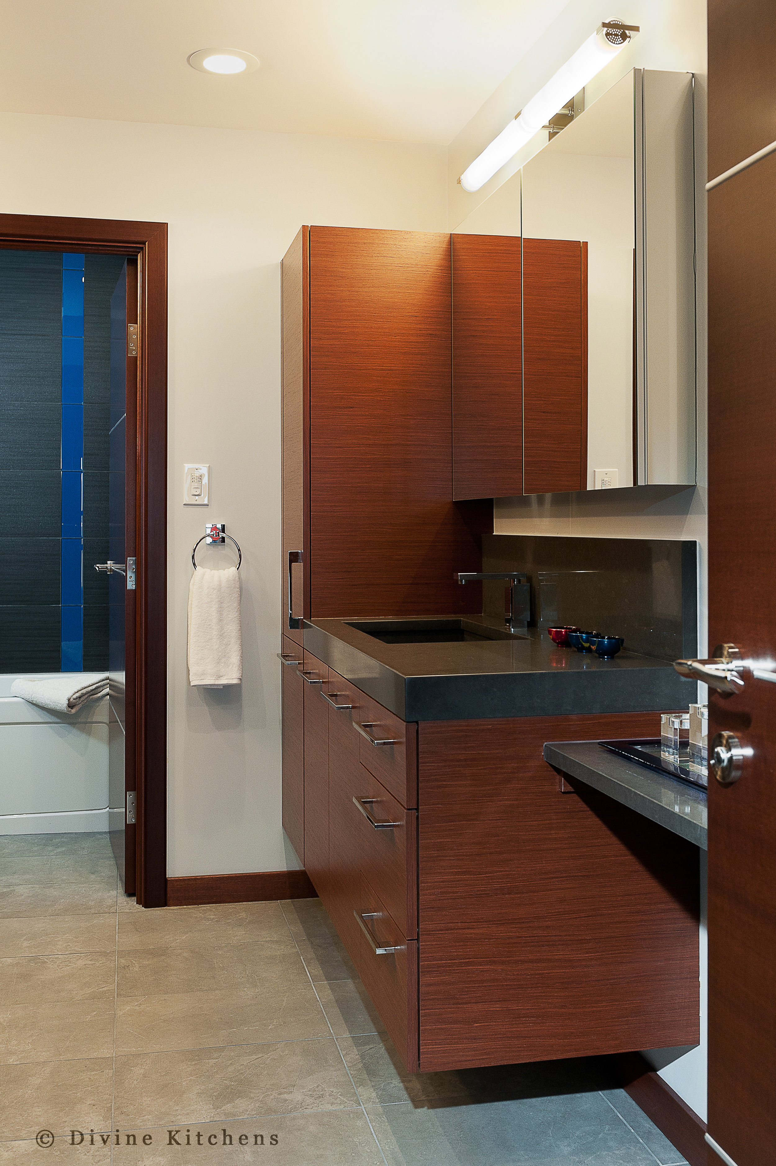 Modern bathroom with cherry veneer cabinets and slate tile shower and bathroom floors. Granite countertop and sink basin. Blue tile accents.