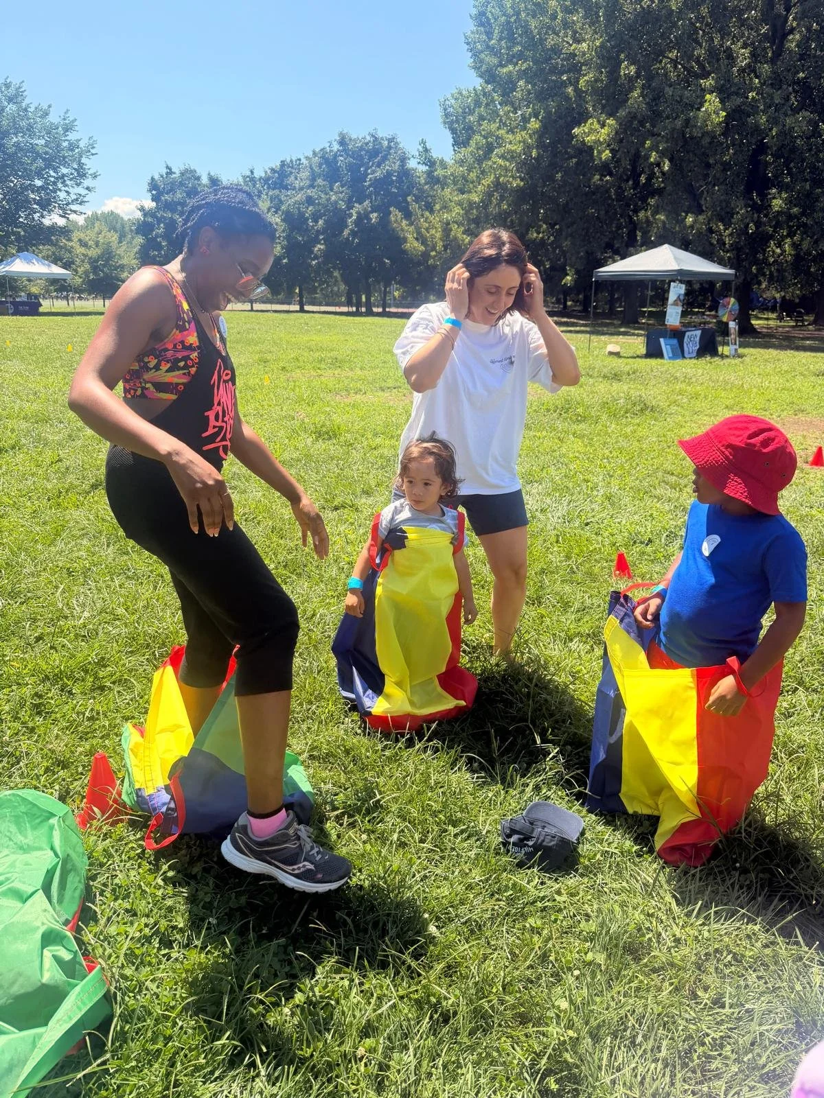 Two small children and two women prepare for Lessons to Blessings Family Field Day Potato Sack Race in a grassy field