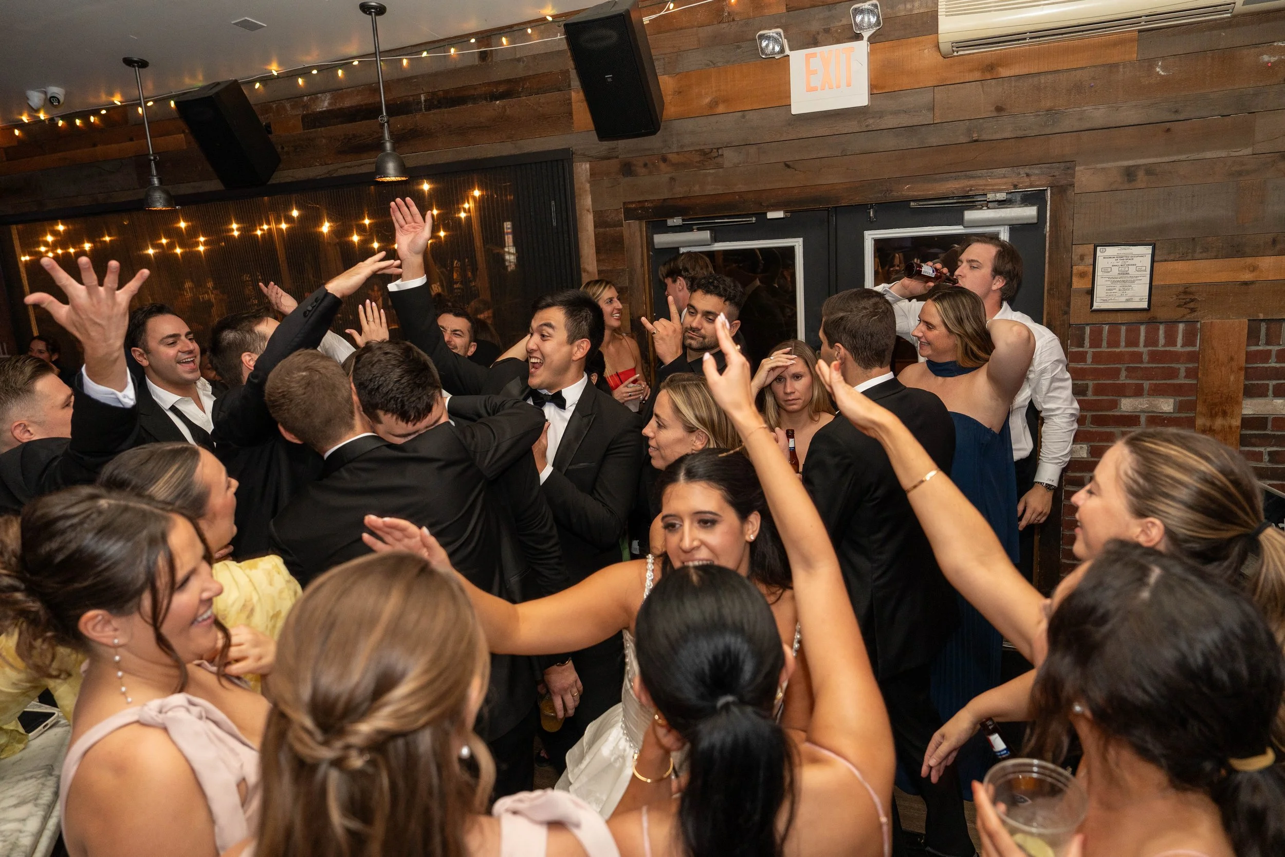 People celebrating at a party, dancing, and having fun in a room with brick walls and string lights.