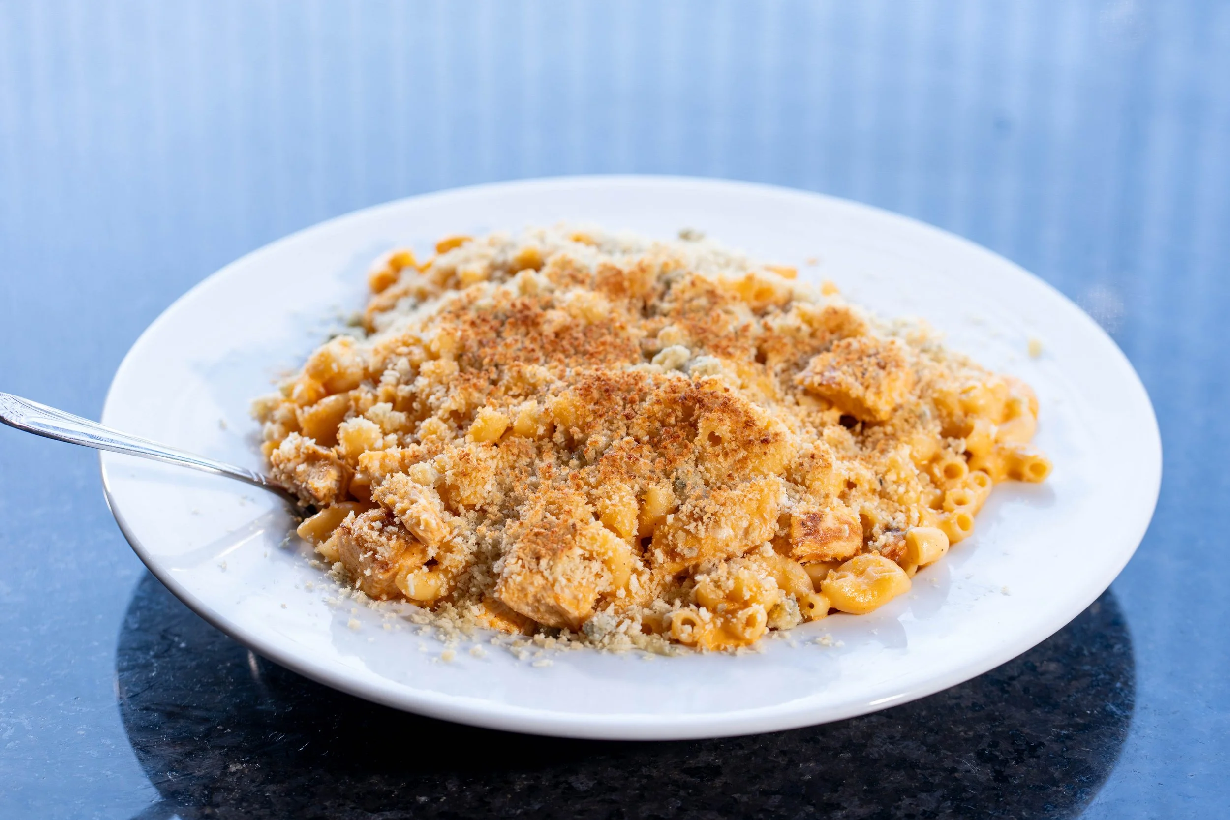 A white plate of baked macaroni and cheese with a breadcrumb topping on a dark countertop.
