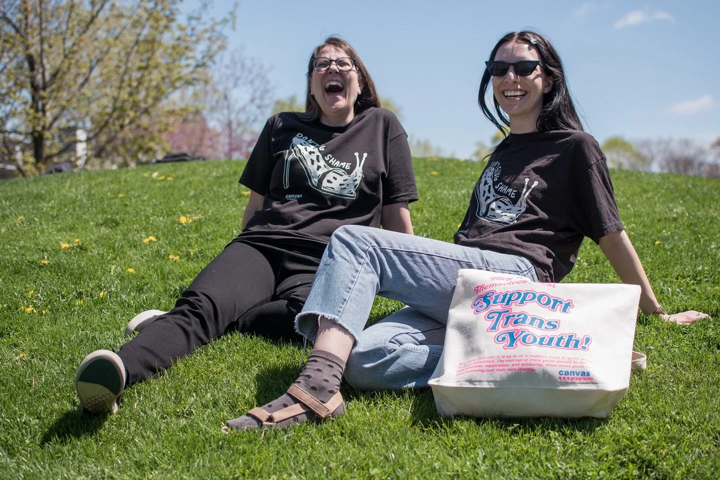 Two smiling slugs sitting in the sun! (Also ft. Our Support Trans Youth tote bag) . Get your shirt + tote on our Canvas Corner Store page. Show us how you slug slayyy!