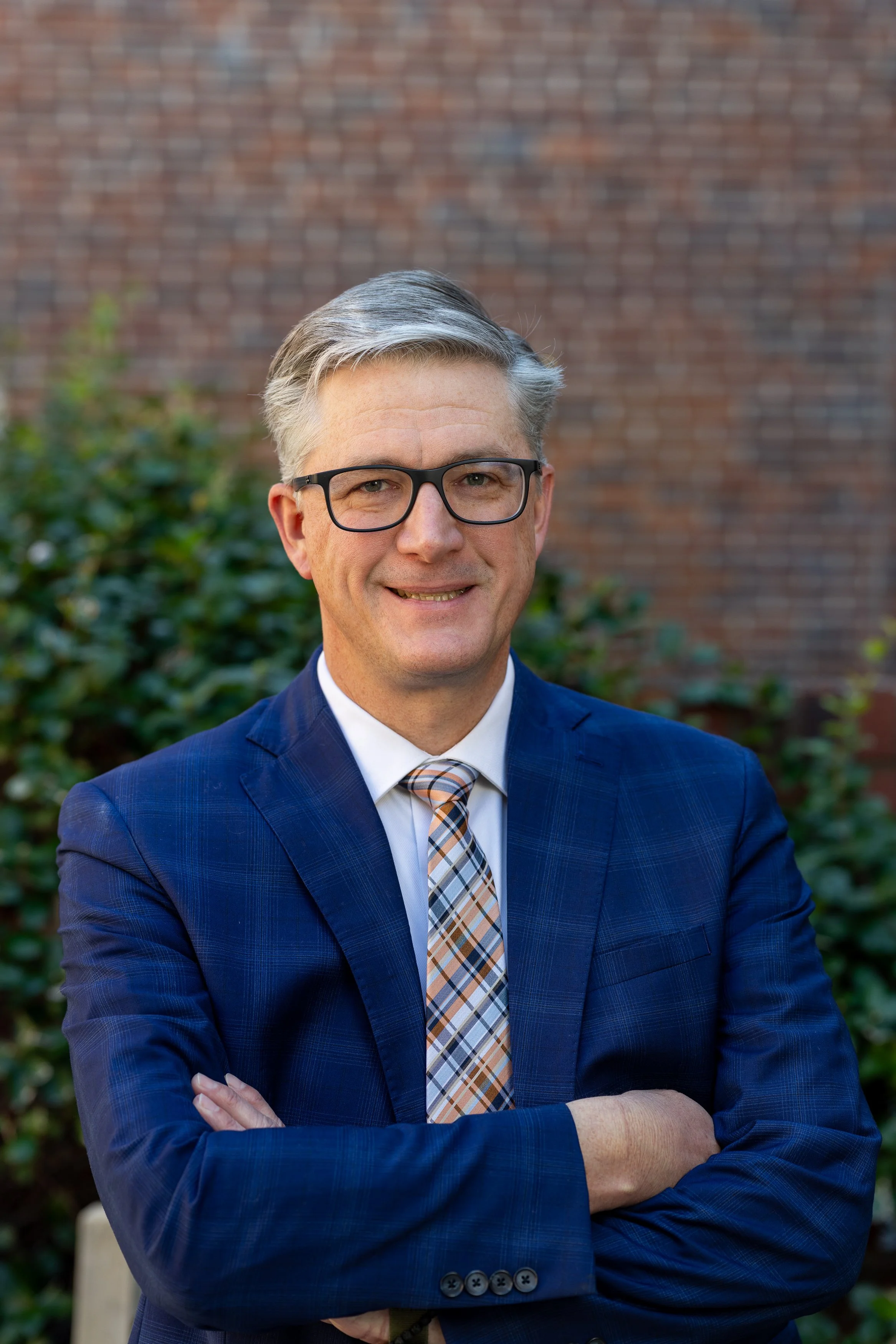 Smiling man with glasses in front of a stained glass window, wearing a suit and tie.