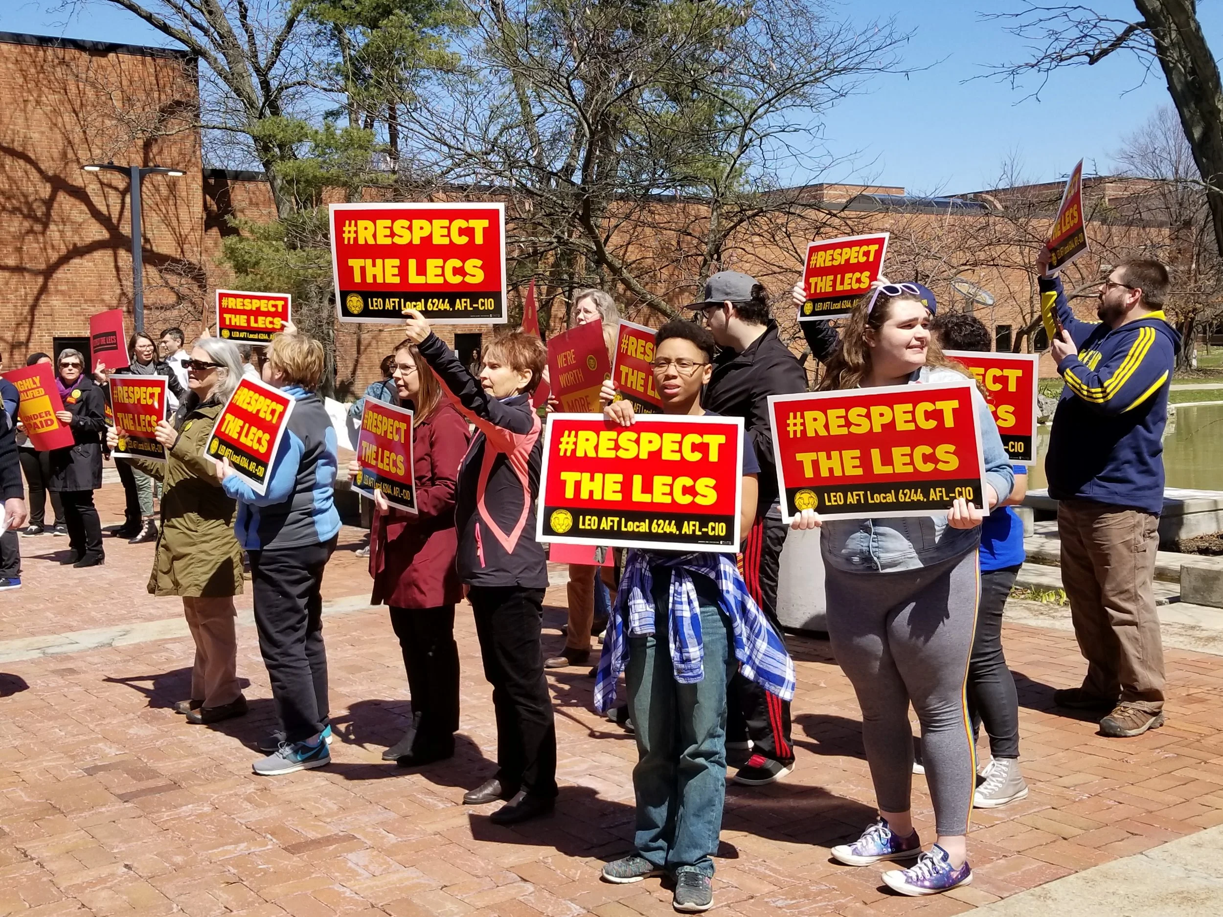 A group of LEO lecs and student allies hold aloft signs that read #Respect The Lecs.