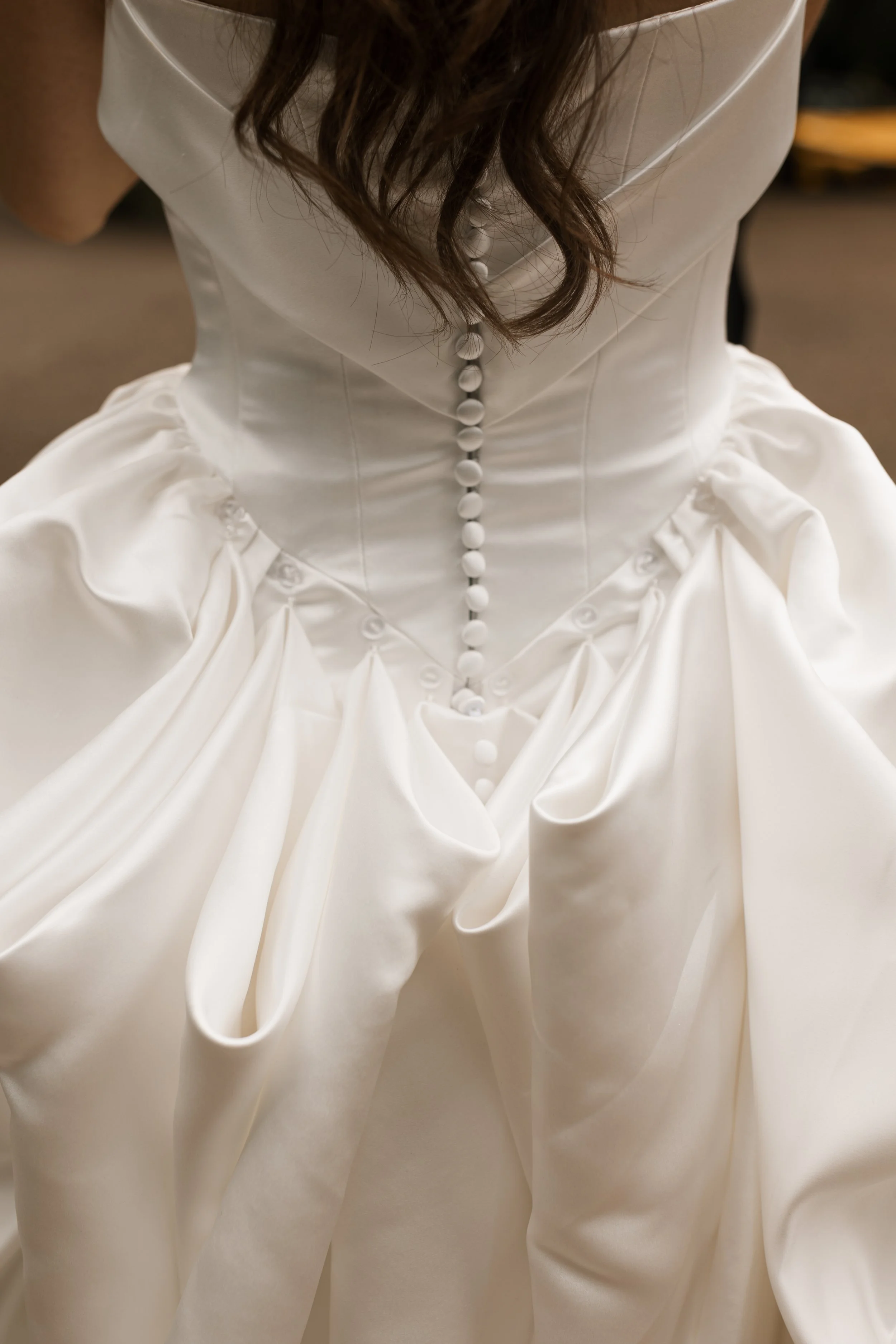 Close-up of a white wedding dress with a fitted bodice and buttons down the back, featuring a voluminous skirt with pleats and ruffles.