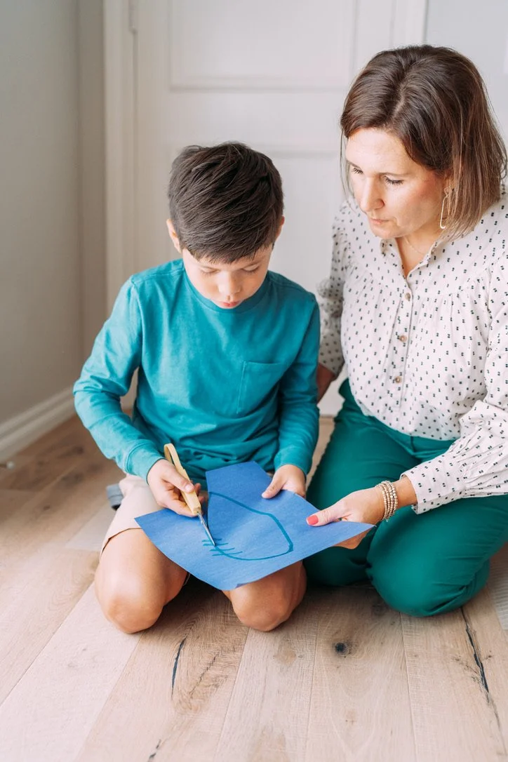 Young boy with occupational therapist practice his skills to cut paper.